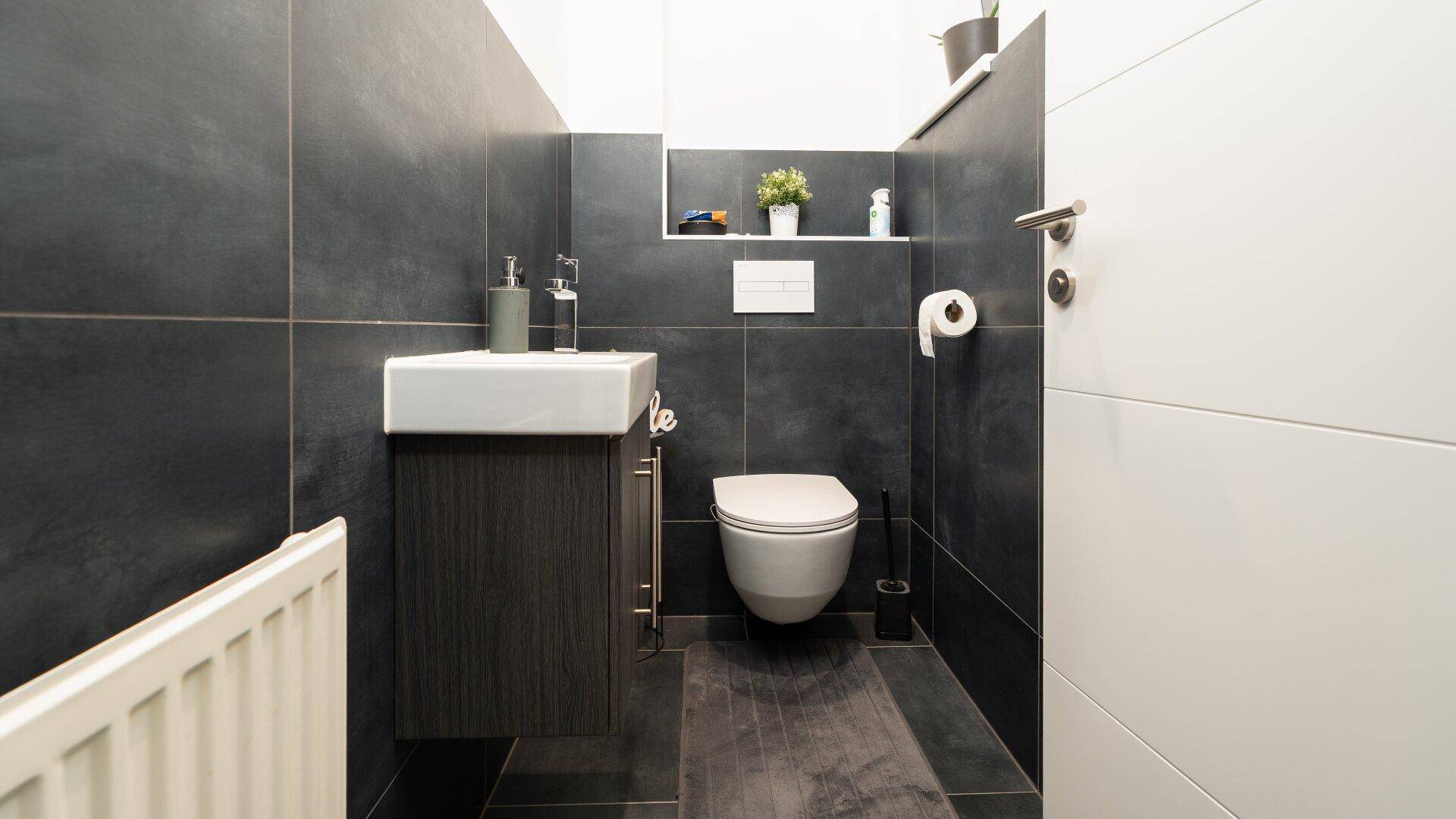 Modernes Gäste-WC mit dunklen Fliesen, wandhängendem WC und kleinem Waschbecken.