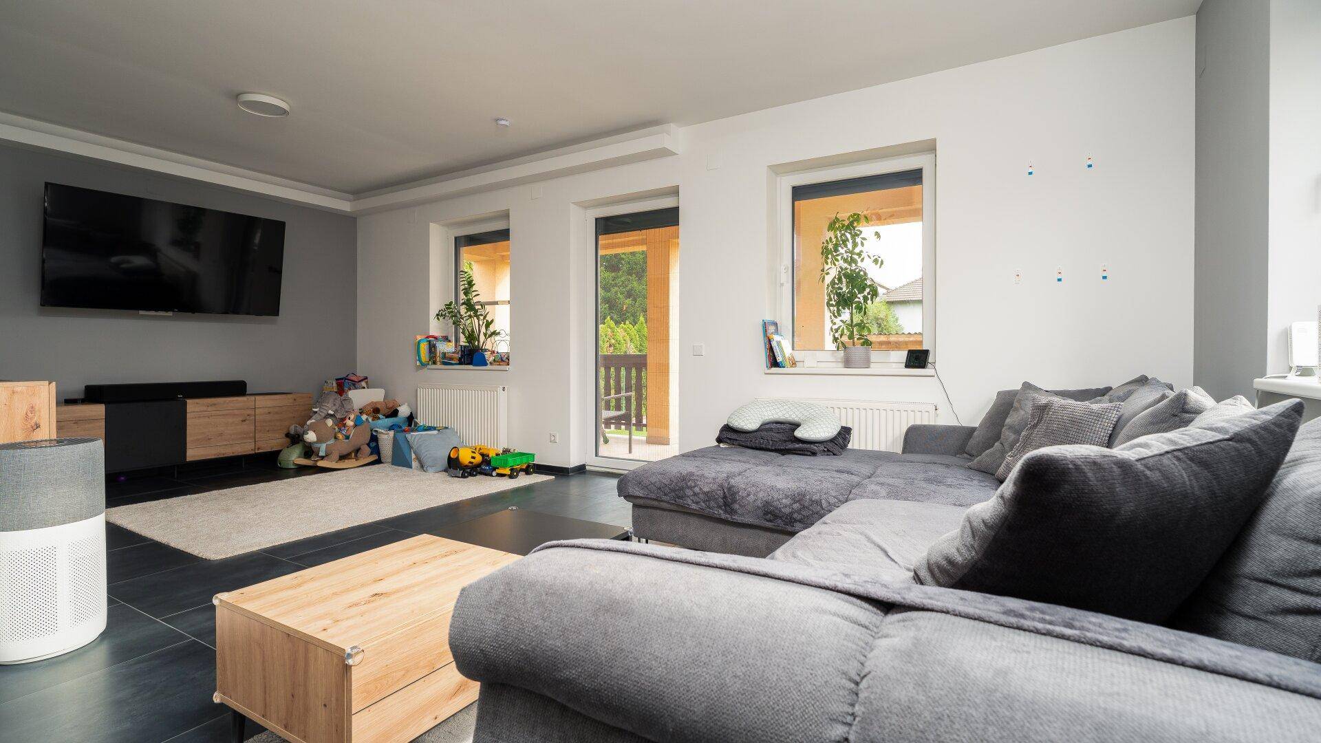 Geräumiges Wohnzimmer mit großem Ecksofa, Fliesenboden und Zugang zu einem Balkon.