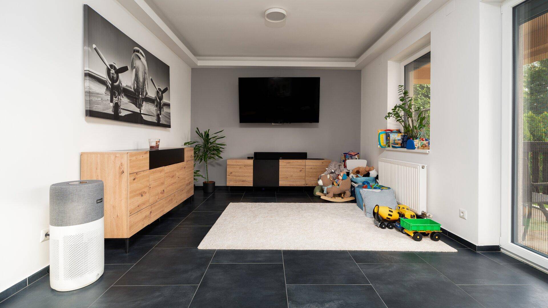 Helles Wohnzimmer mit Fliesenboden, TV-Bereich und modernen Holzmöbeln.