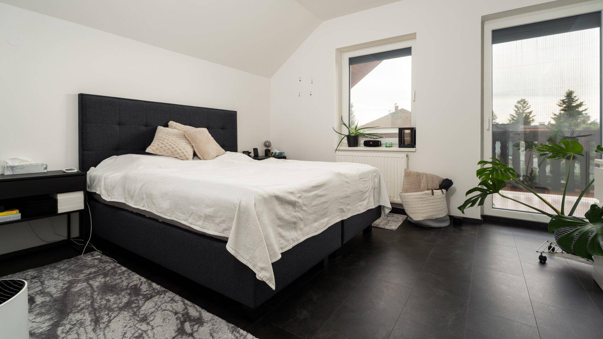 Schlafzimmer mit großem Bett, dunklem Boden und Zugang zu einem Balkon.
