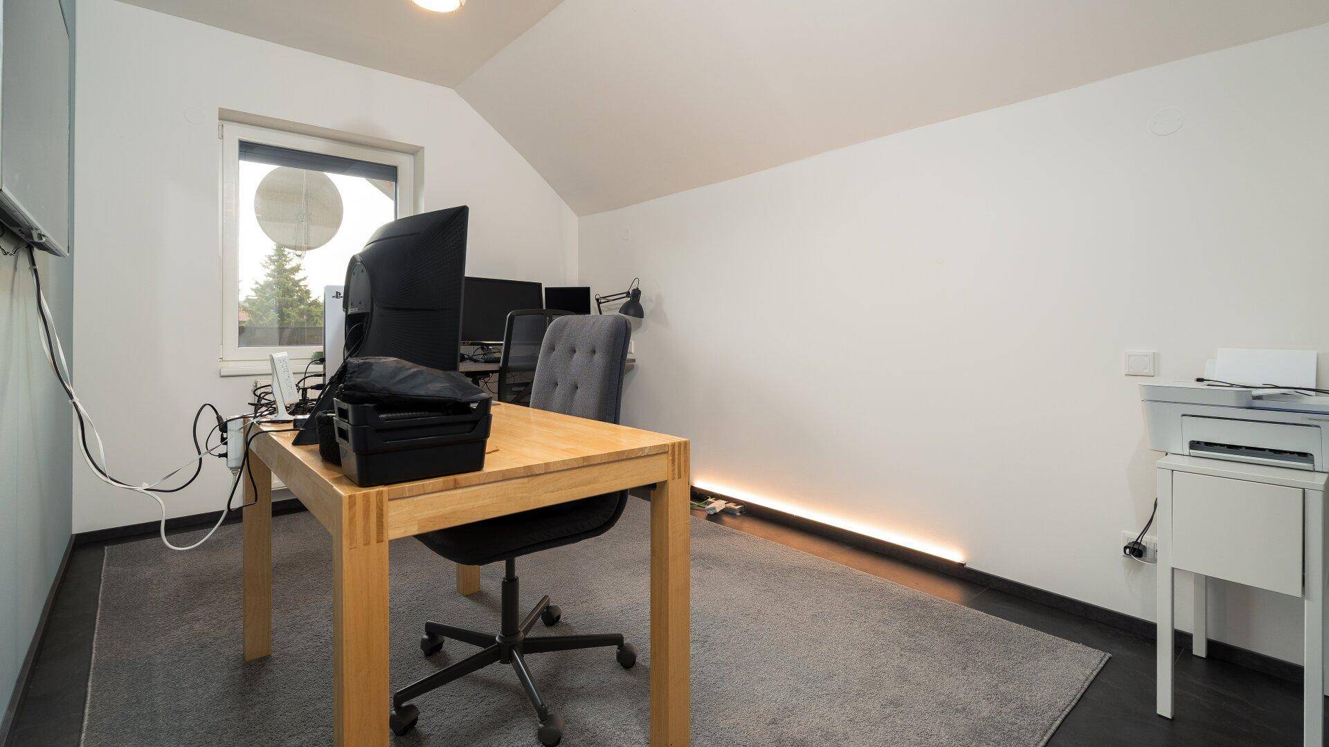 Helles Arbeitszimmer mit Schreibtisch, Computer und schrägen Wänden unter dem Dach.