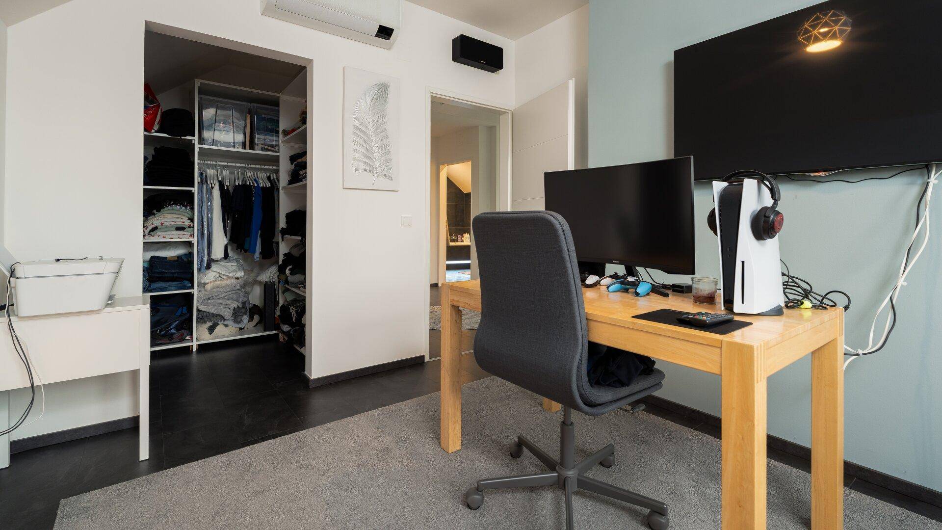 Arbeitszimmer mit Schreibtisch, Computer und offenem Zugang zu einem begehbaren Kleiderschrank.