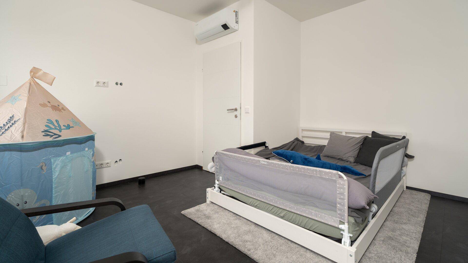 Kinderzimmer mit Kinderbett, Spielzelt und Klimaanlage an der Wand.