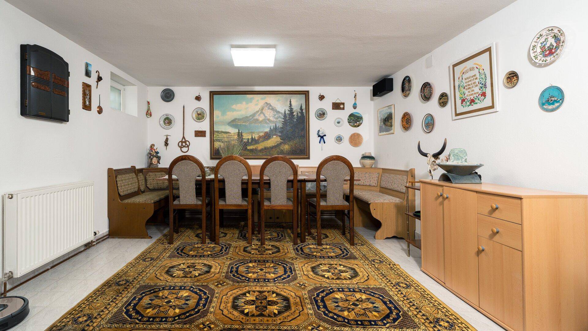 Geräumiger Kellerraum mit großem Esstisch, Sitzbänken und traditionellem Teppich.
