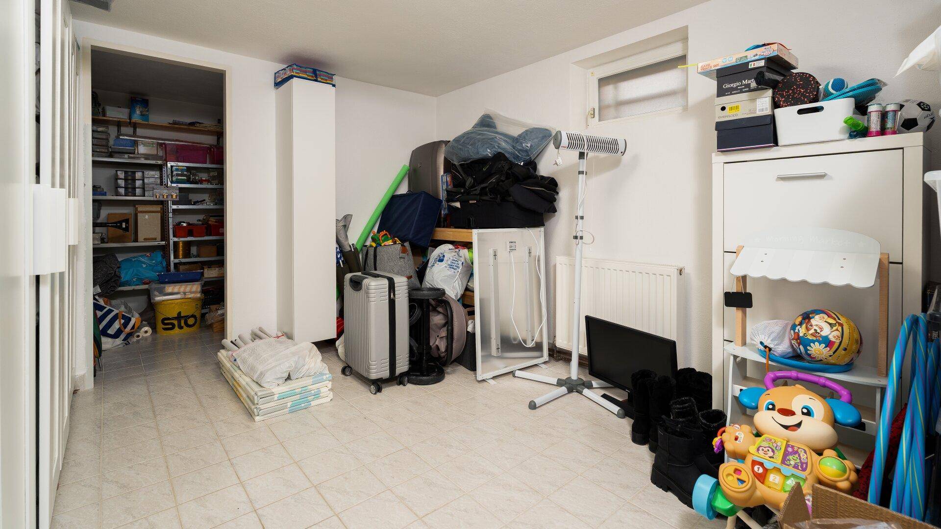 Unaufgeräumter Abstellraum im Keller mit Regalen und verschiedenen Haushaltsgegenständen.