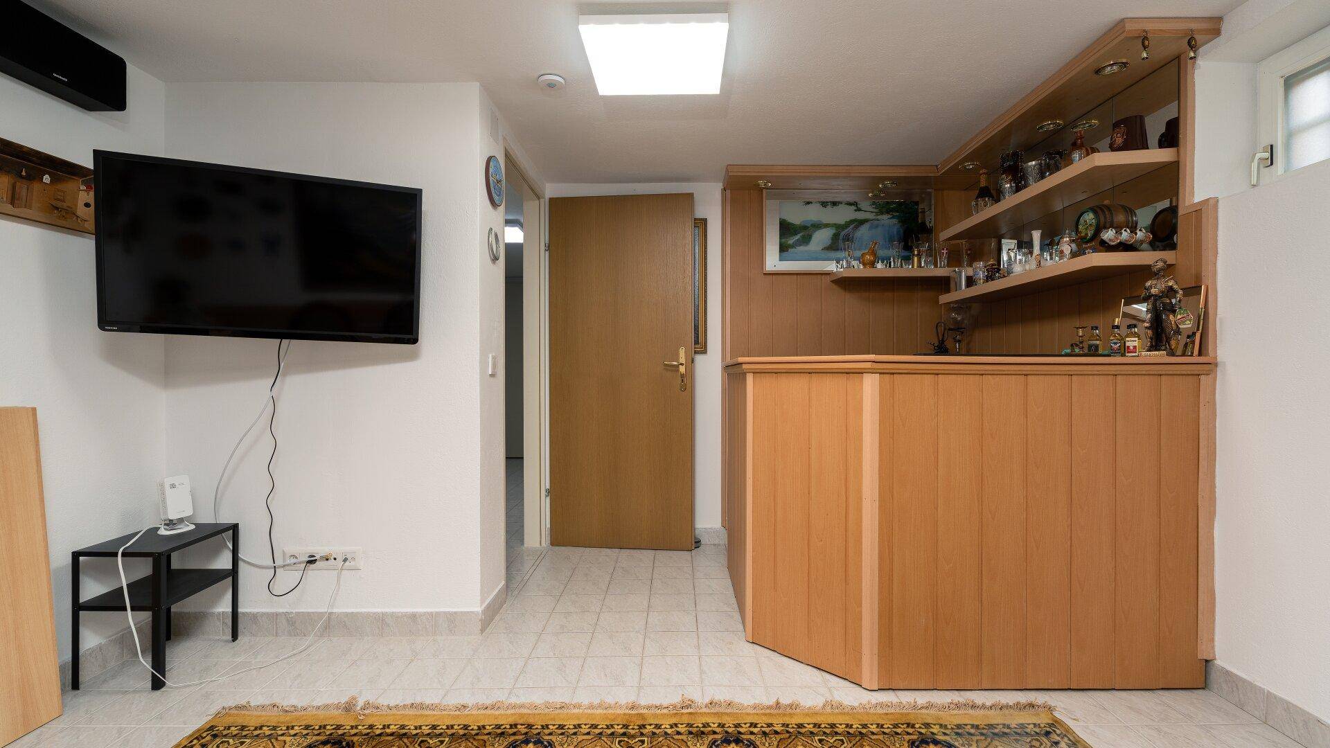 Kellerraum mit Bar, Fernseher und Zugang zu weiteren Räumen im Untergeschoss.