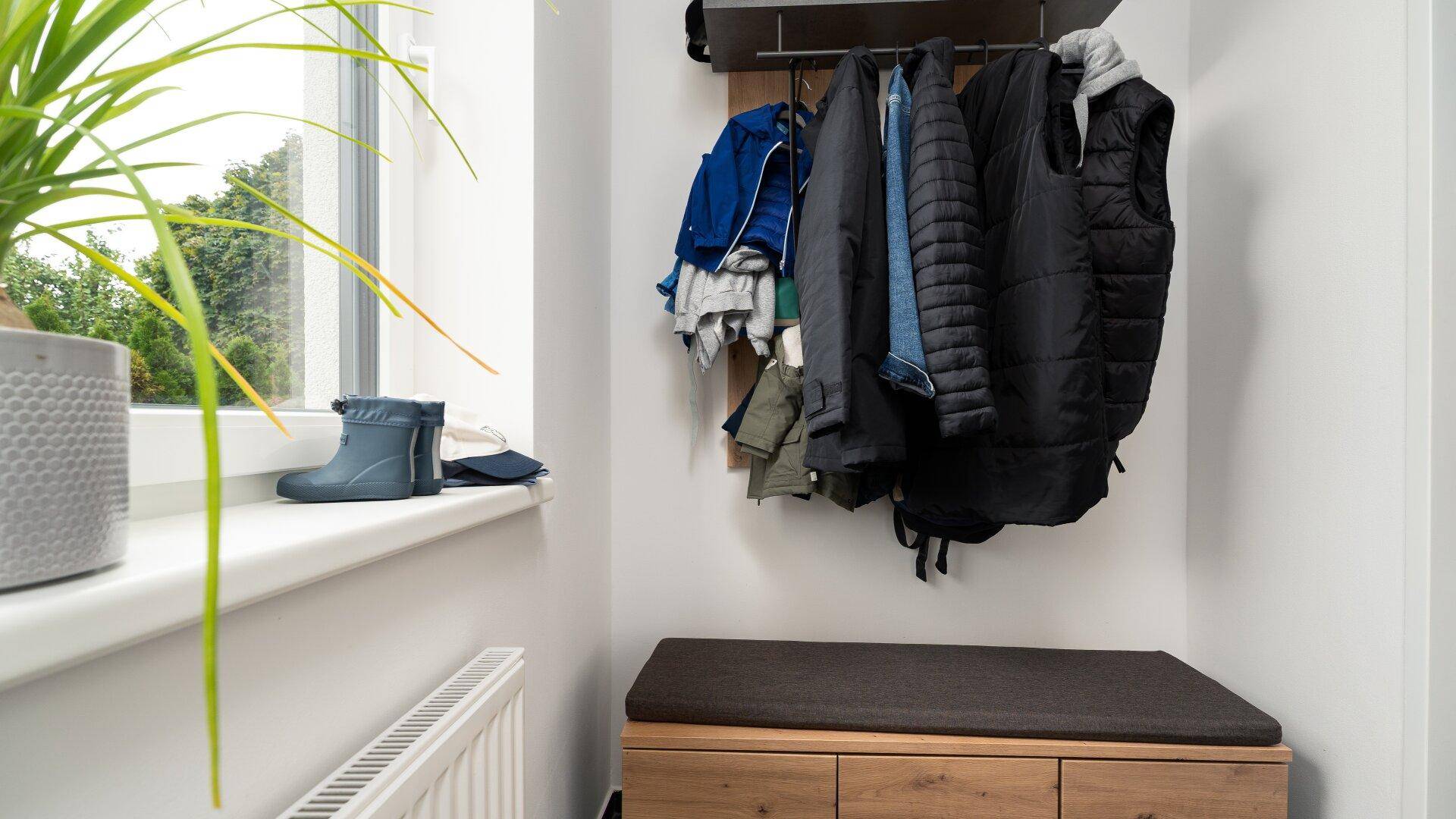 Eingangsbereich mit Garderobe, Sitzbank und einem Fenster, das natürliches Licht hereinlässt.