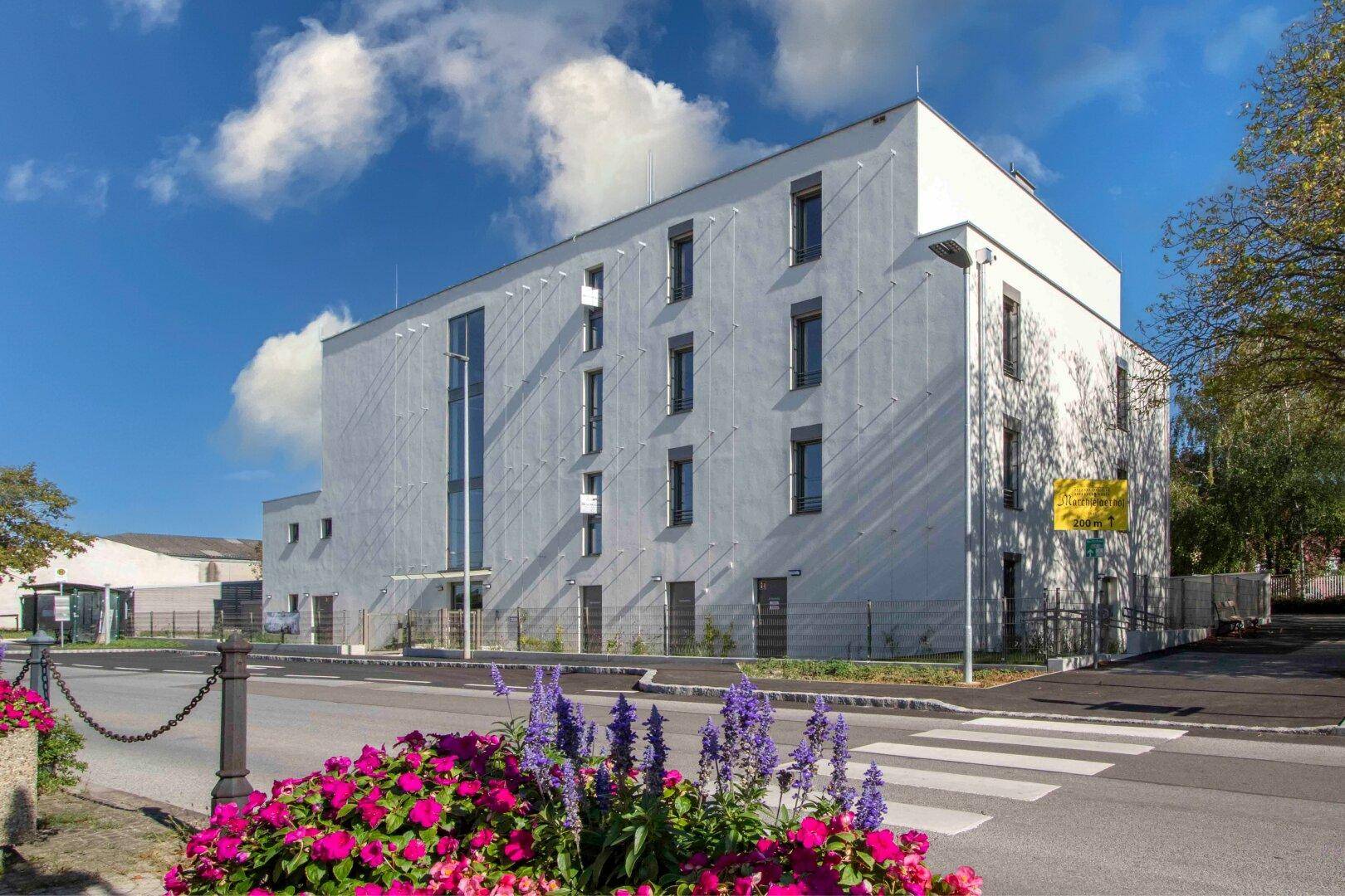Moderne Wohnanlage mit weißer Fassade und großen Fenstern, umgeben von Blumenbeeten.
