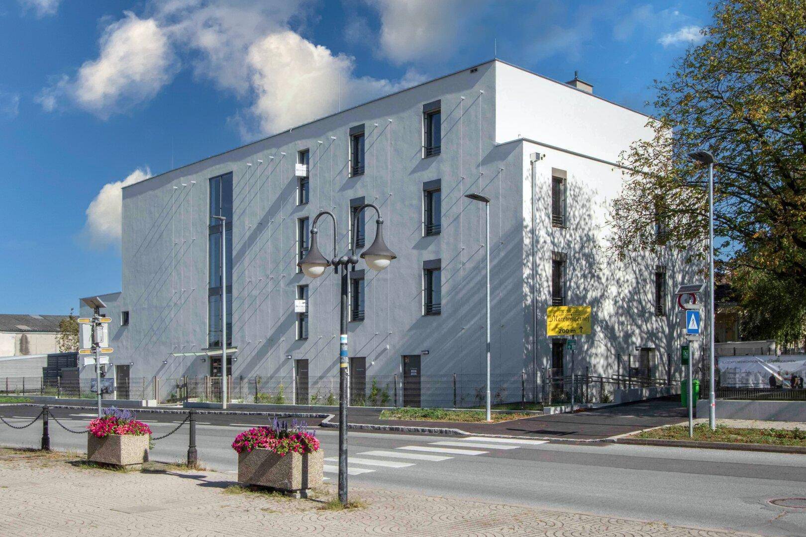 Ansicht der modernen Wohnanlage mit weißer Fassade, großen Fenstern und Straßenlaternen.