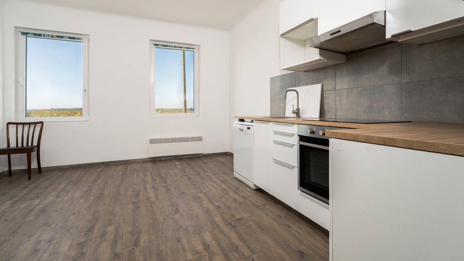 Moderne Einbauküche mit weißen Schränken, Holzarbeitsplatte und Blick ins Grüne.