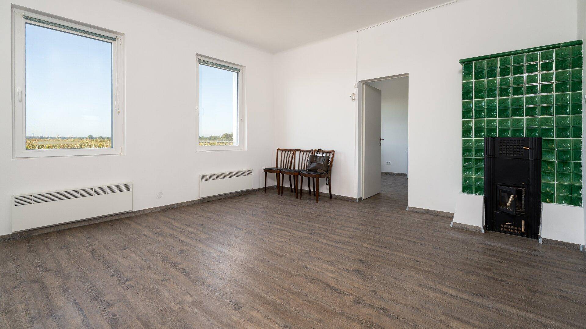 Helles Wohnzimmer mit Laminatboden und einem traditionellen grünen Kachelofen als Blickfang.