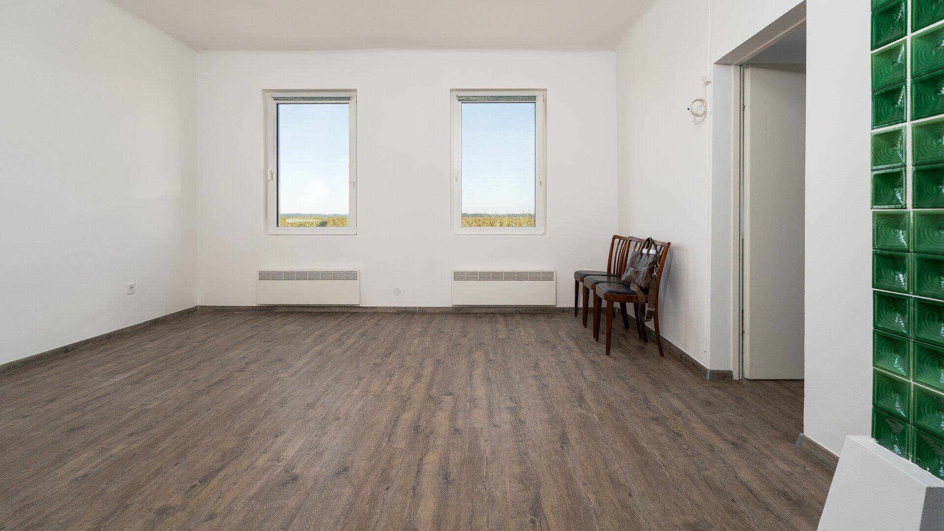 Geräumiges Wohnzimmer mit Laminatboden, weißen Wänden und zwei großen Fenstern.