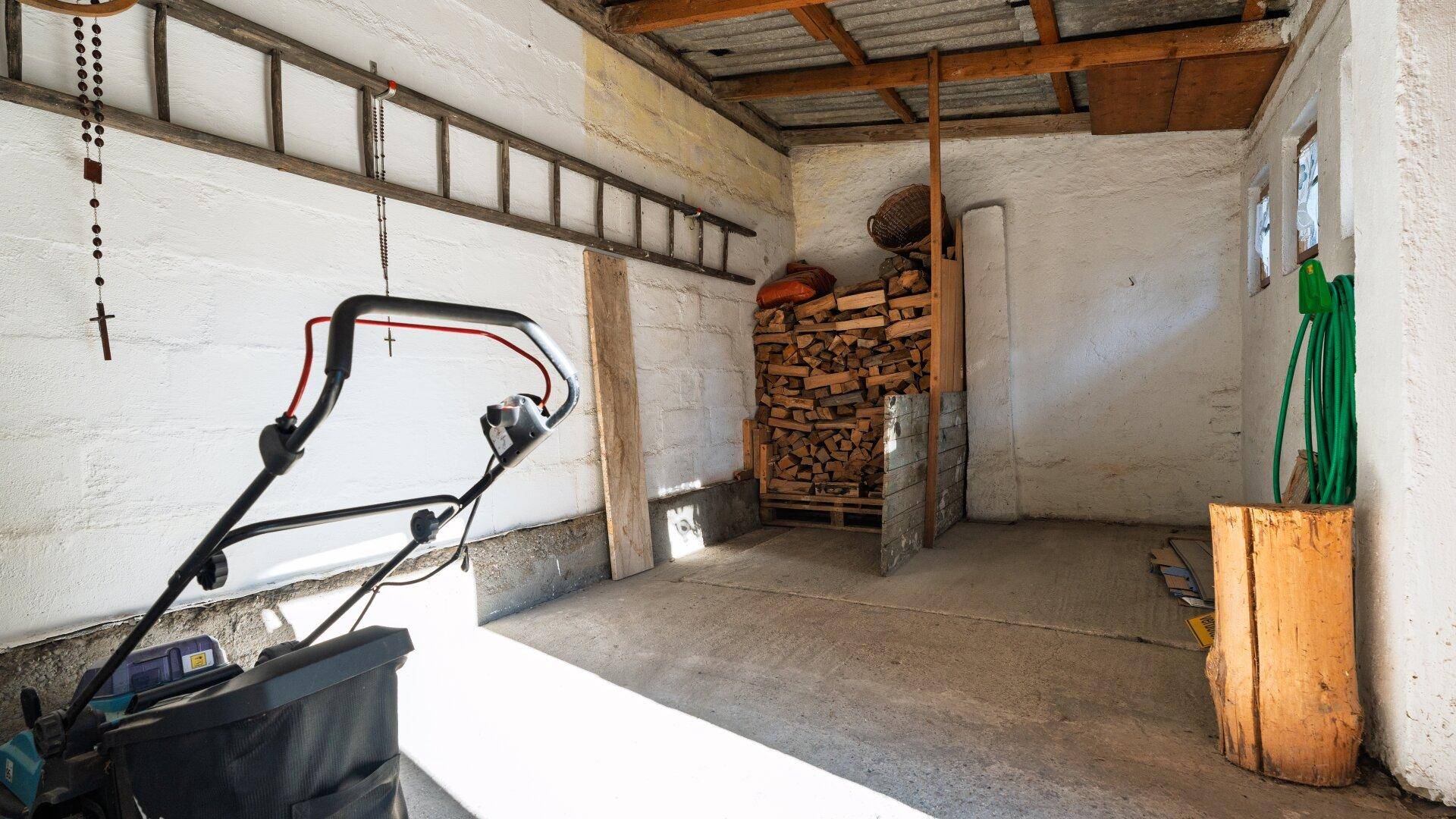 Geräumige Garage mit Betonboden, Holzlager und Gartengeräten.