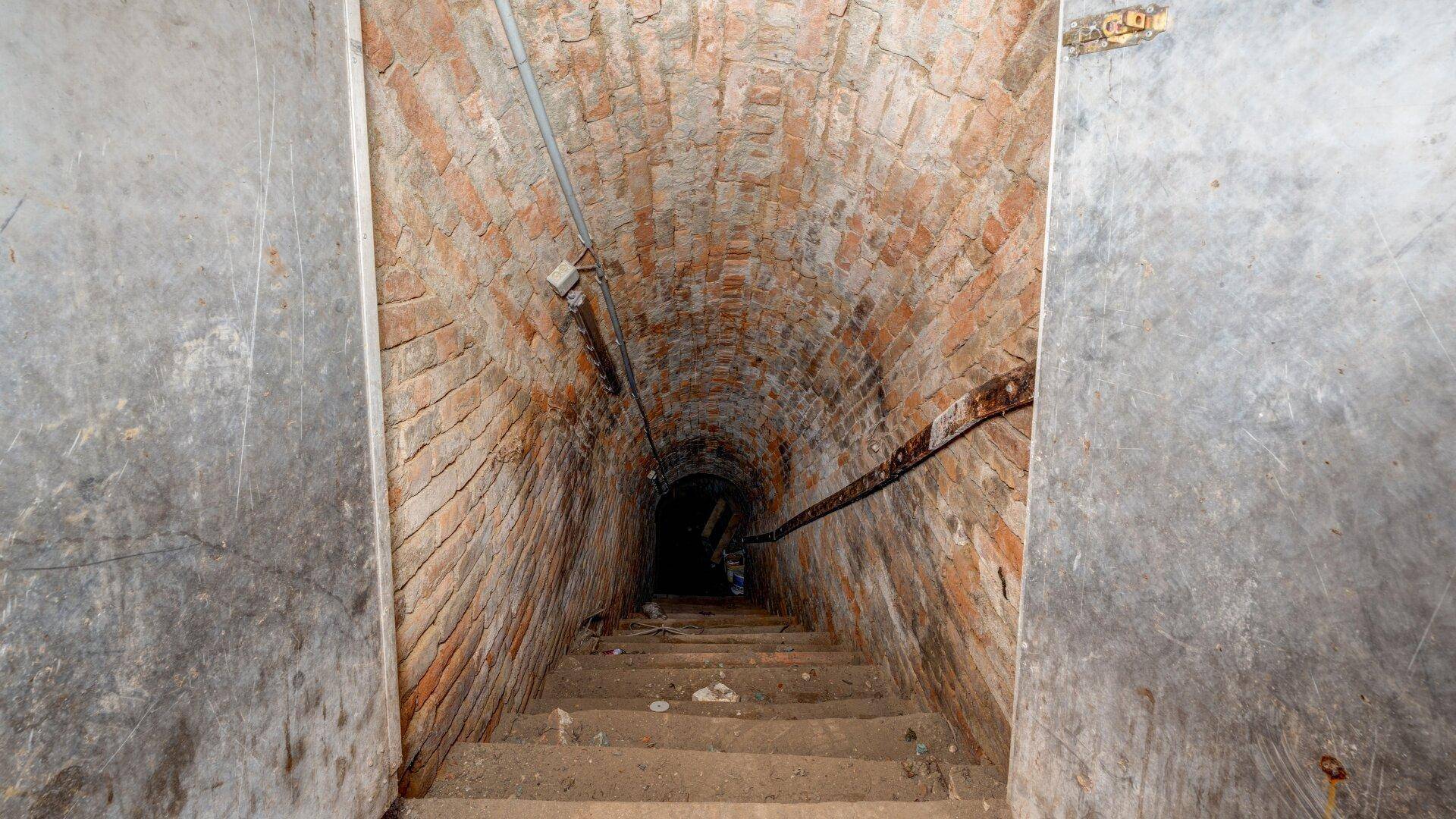 Dunkler, gewölbter Ziegelgang mit Treppen, der tiefer in den Kellerbereich führt.