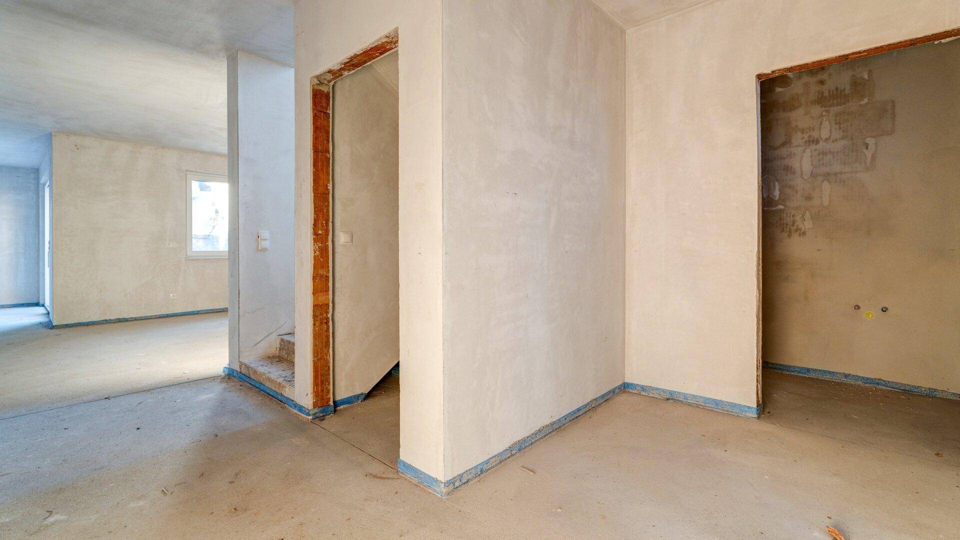 Unfertiger Innenraum mit rohen Wänden und sichtbaren Türrahmen, bereit für den weiteren Ausbau.