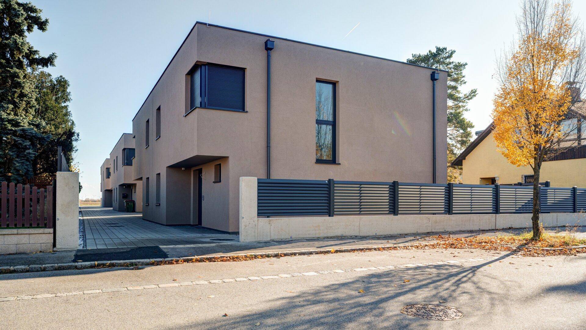 Ansicht der modernen Reihenhäuser von der Straße mit gepflegter Außenanlage und Zaun.