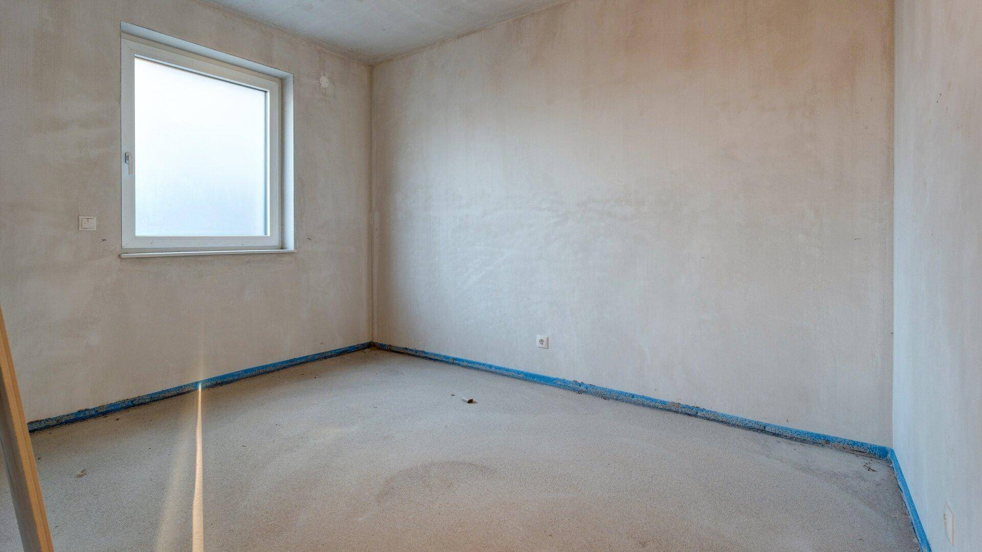 Heller, unfertiger Raum mit einem Fenster, bereit für die individuelle Gestaltung und Nutzung.