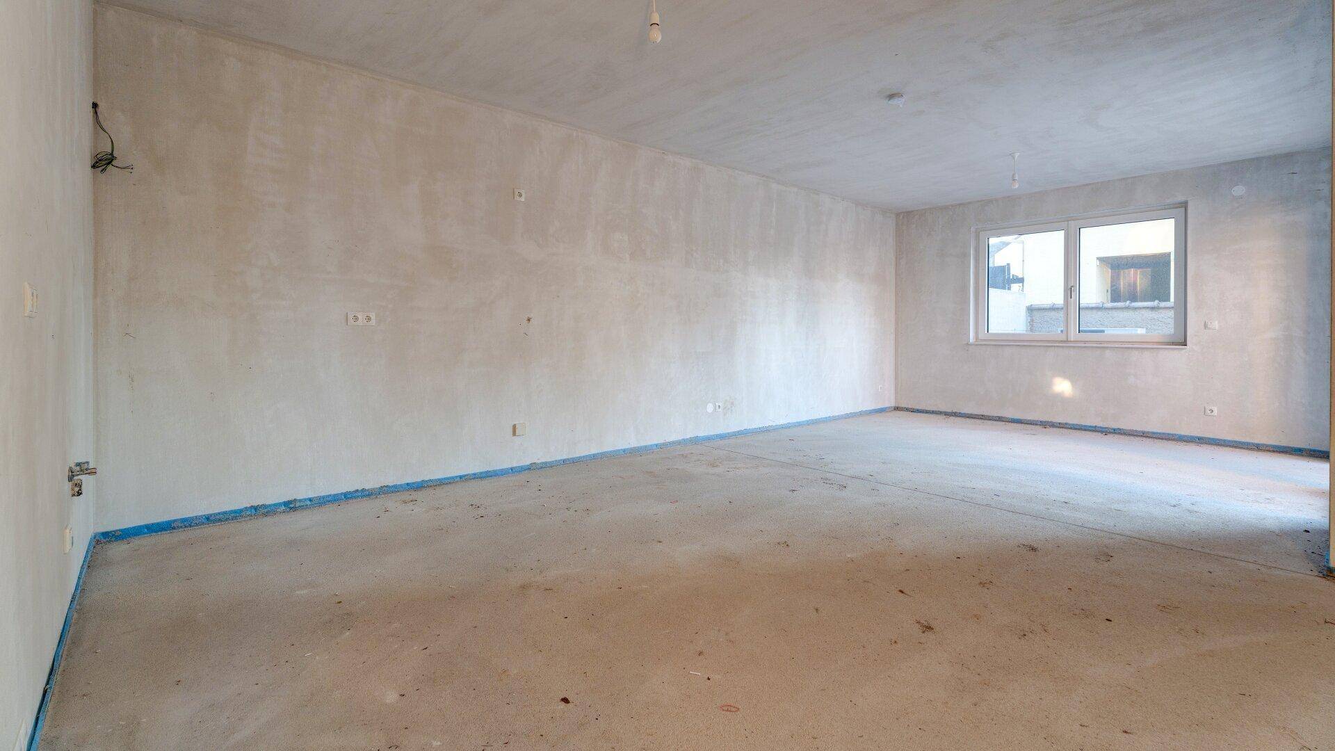 Großer, unfertiger Raum mit einem Fenster, bietet viel Potenzial für individuelle Gestaltung.