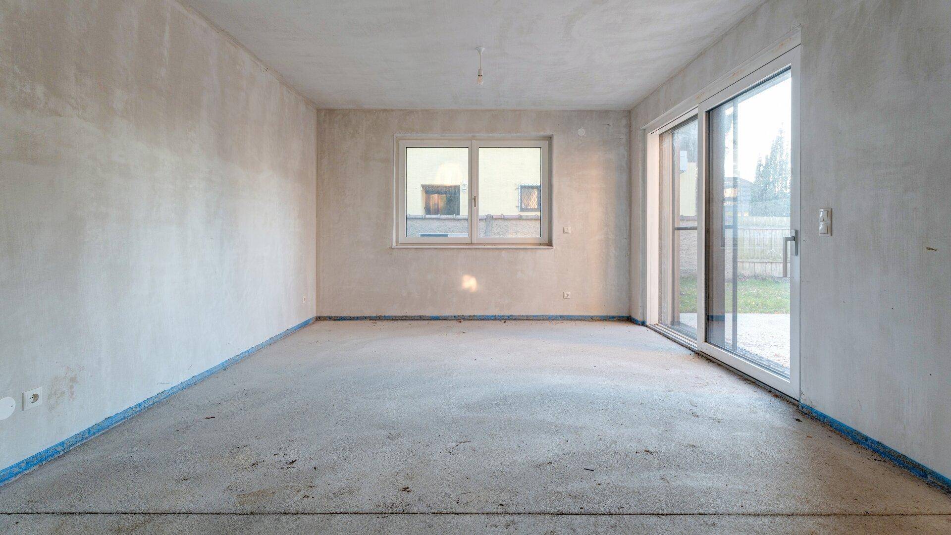 Unfertiger Raum mit Schiebetür zum Außenbereich und einem Fenster, bietet viel Tageslicht.