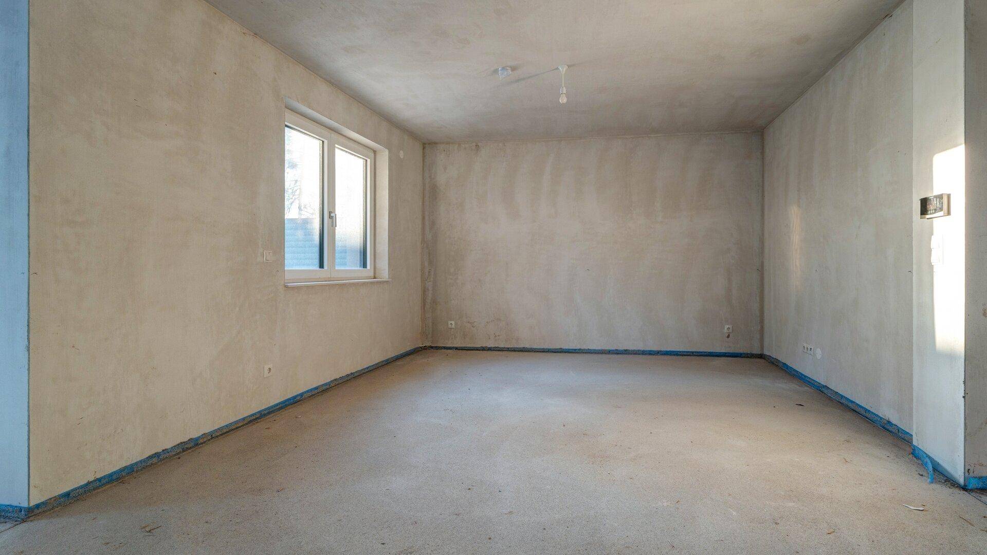 Heller, unfertiger Raum mit einem Fenster, bereit für die individuelle Gestaltung und Nutzung.