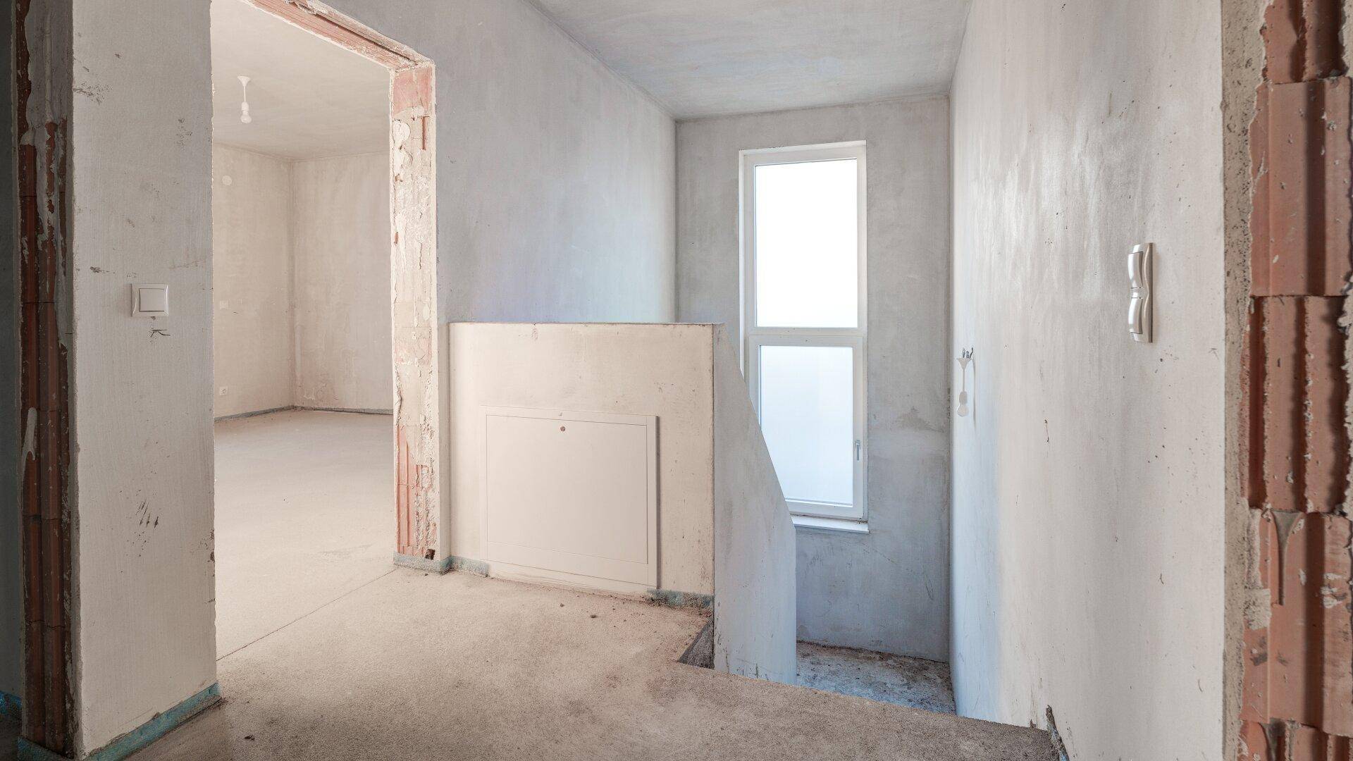 Unfertiger Flurbereich mit Treppenansatz und Fenster, bereit für den weiteren Ausbau.