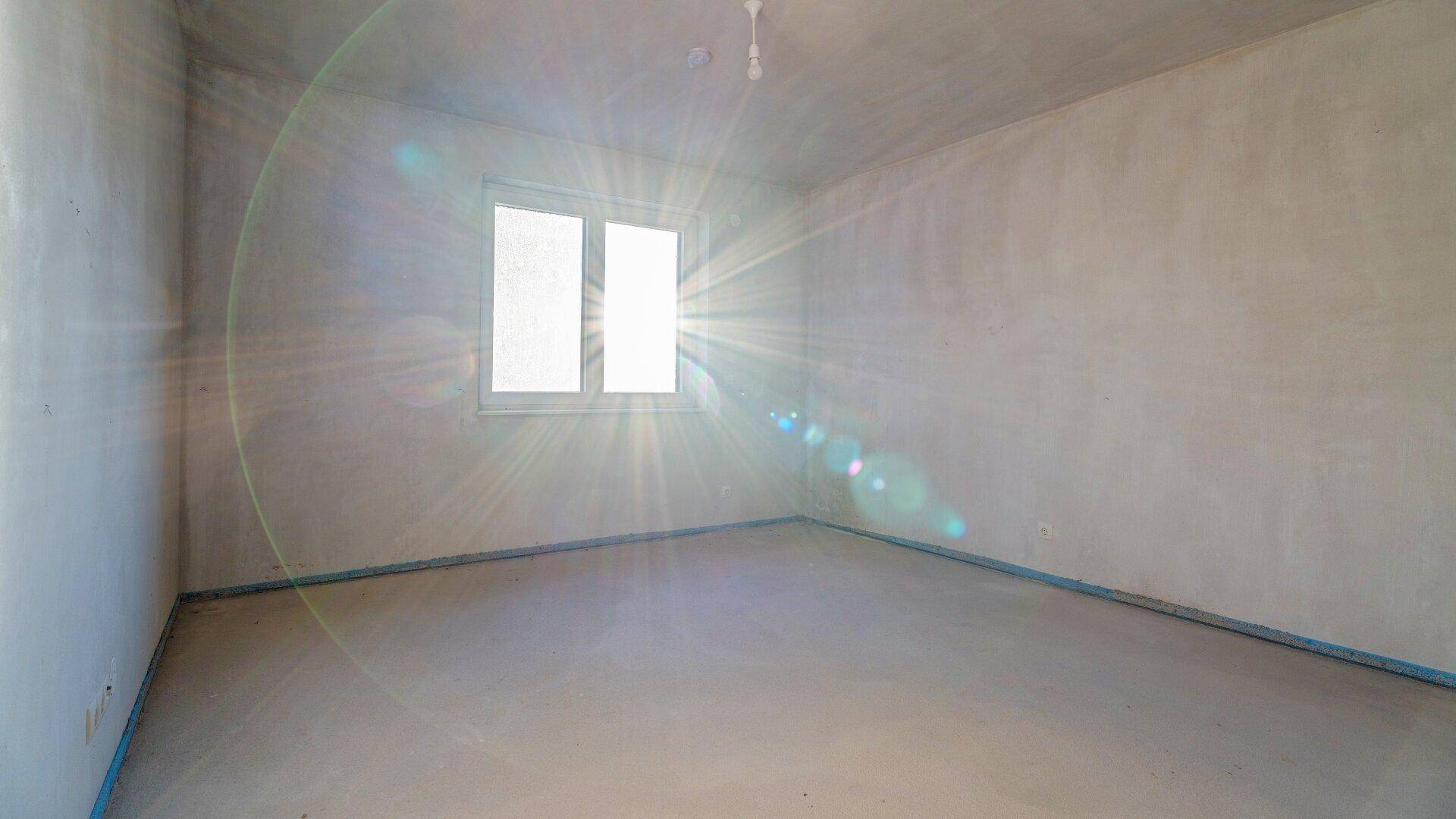 Heller, unfertiger Raum mit starkem Lichteinfall durch das Fenster, bereit für den Ausbau.
