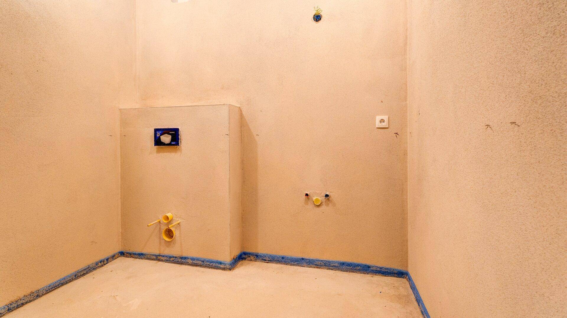 Unfertiger WC-Raum mit sichtbaren Anschlüssen für Toilette und Waschbecken.