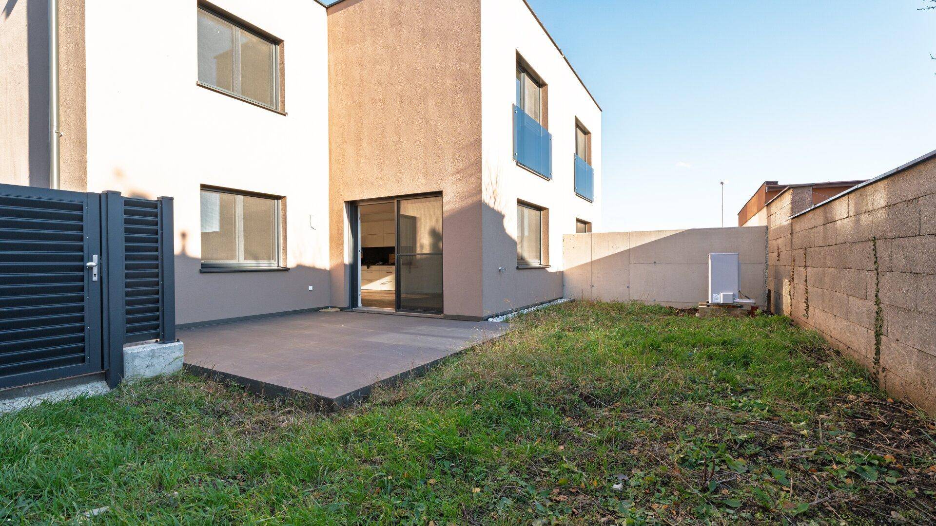 Rückseite des Hauses mit Terrasse und Gartenbereich, umgeben von einer Mauer.