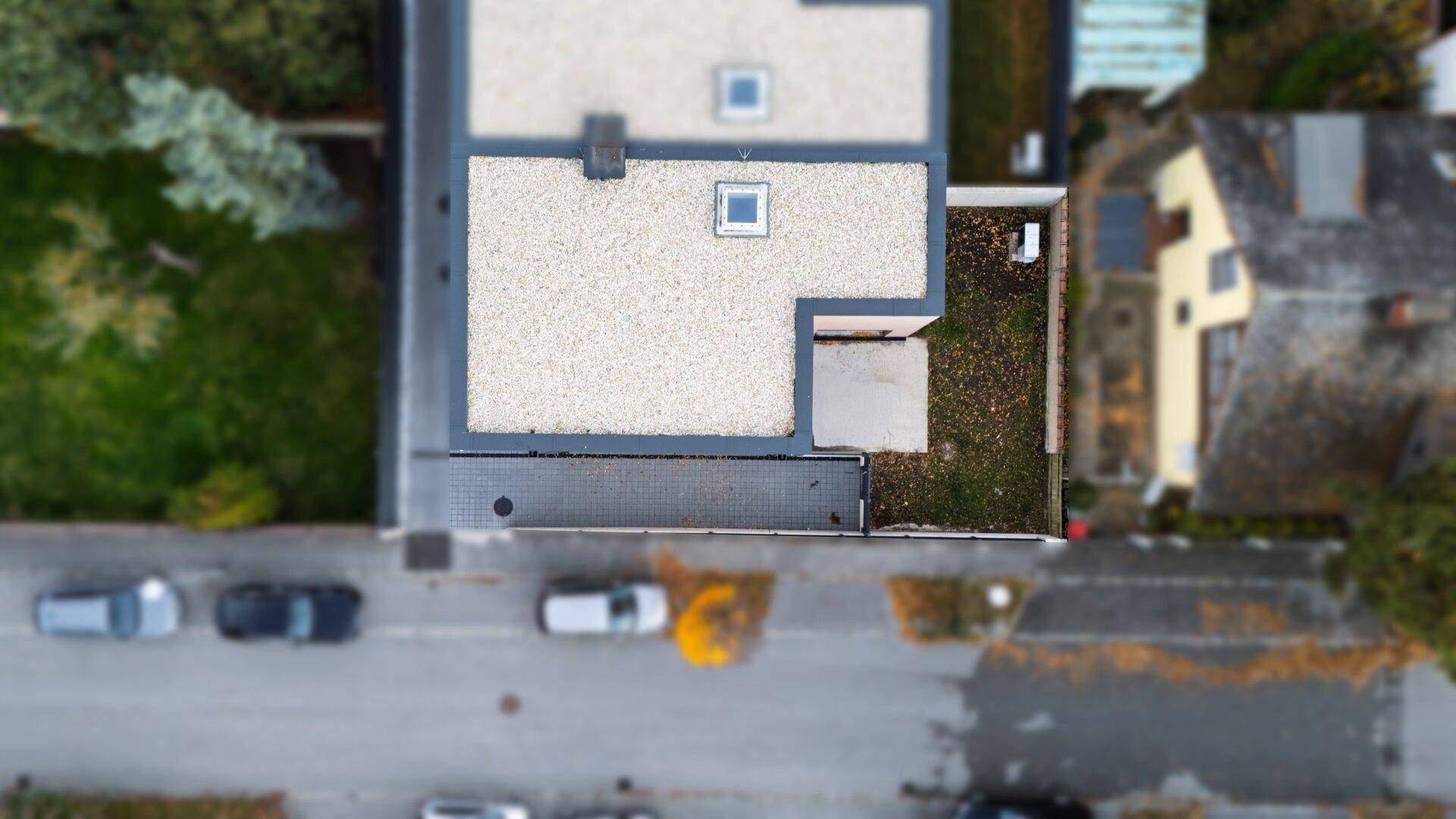 Draufsicht auf das Flachdach des Hauses mit Oberlicht und angrenzendem Gartenbereich.