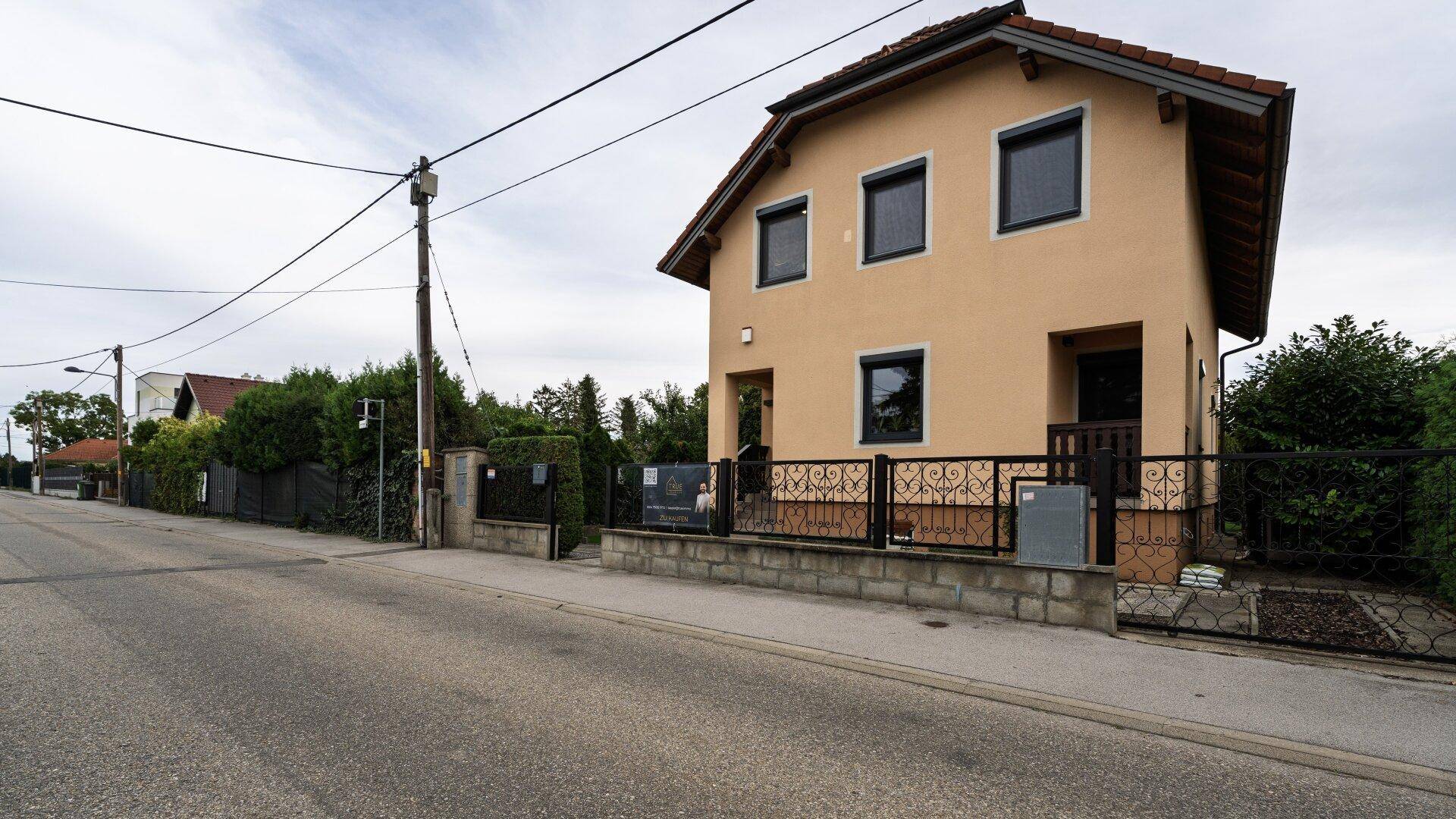 Ansicht des Hauses von der Straße mit Zaun und Einfahrt.