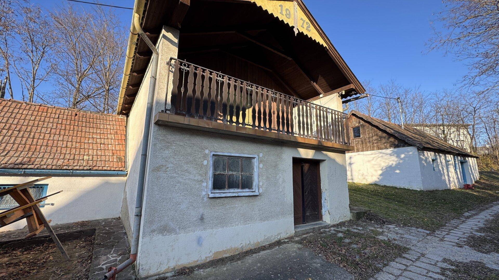 Ansicht des alten Landhauses mit Balkon und traditionellem Geländer unter strahlendem Sonnenschein.
