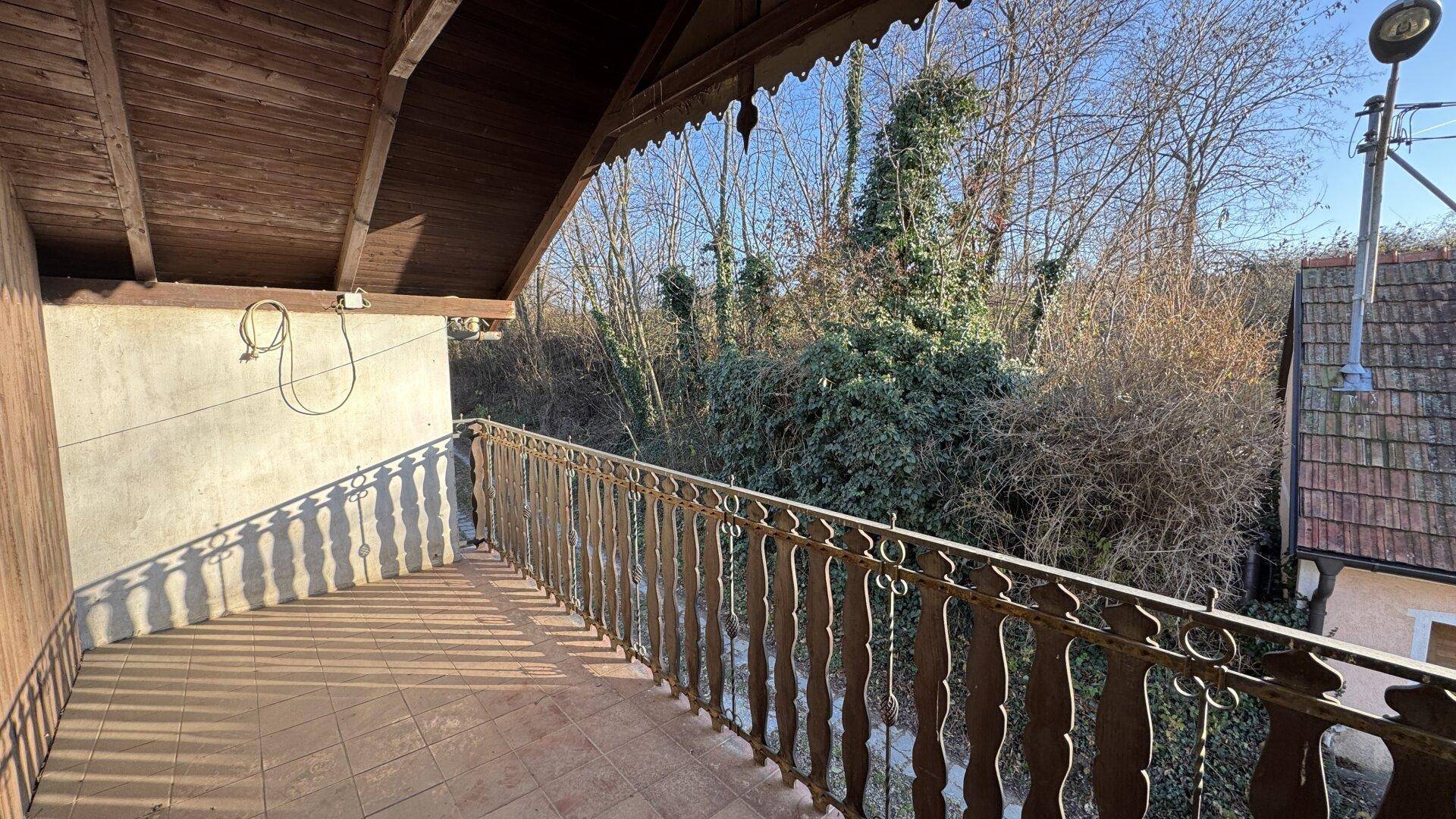Überdachter Balkon mit traditionellem Holzgeländer und Blick ins Grüne.