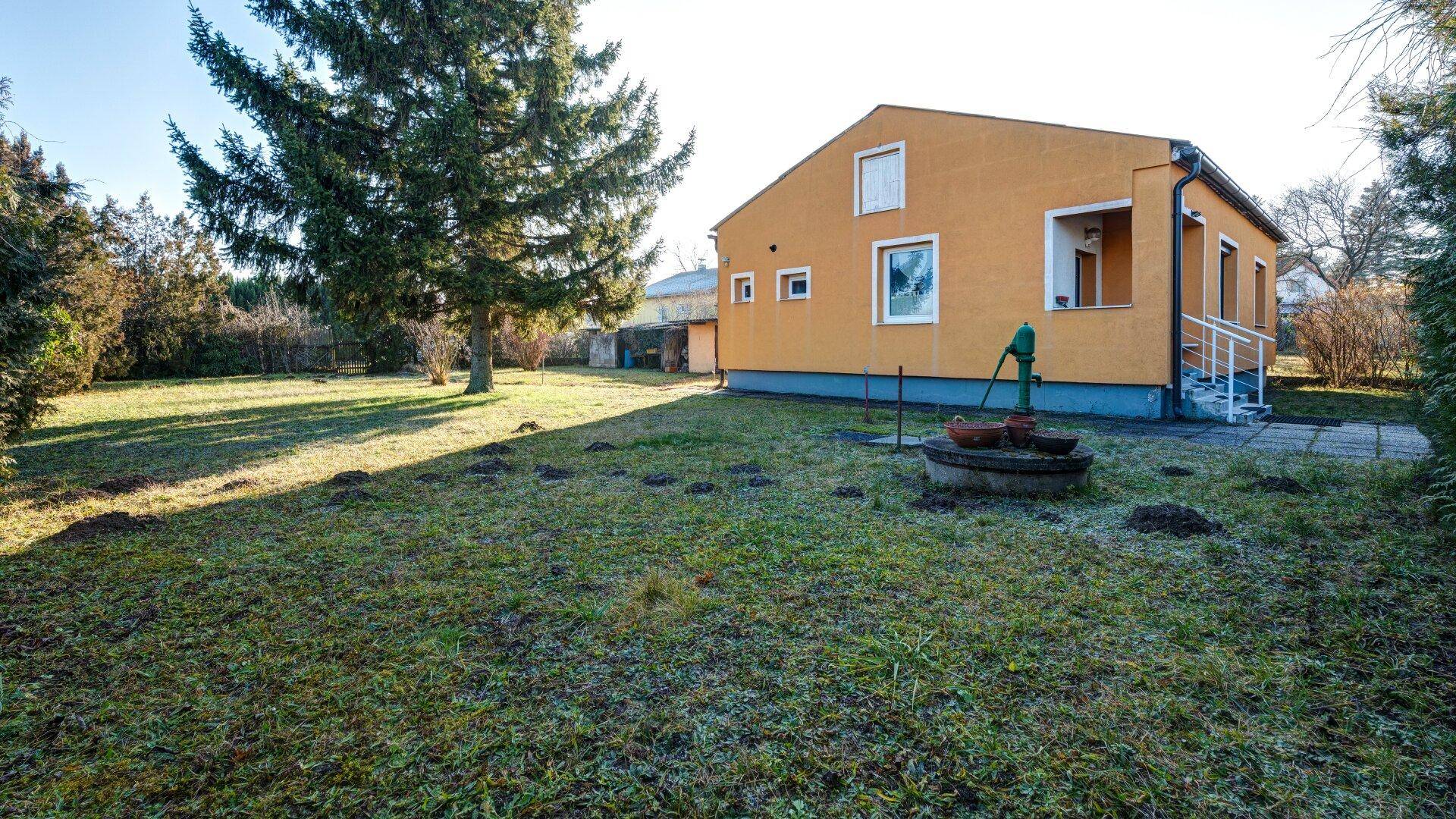 Seitenansicht des Hauses mit einem Brunnen im Vorgarten und weitläufiger Rasenfläche.