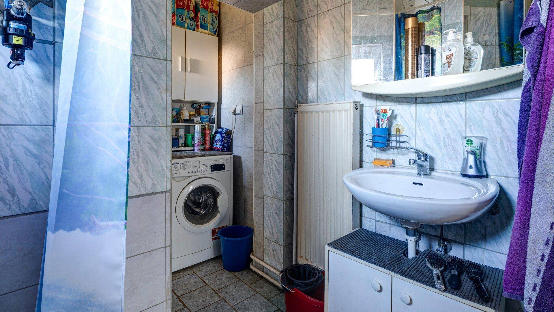 Badezimmer mit Waschbecken, Heizkörper und Waschmaschine, alles in funktionalem Zustand.
