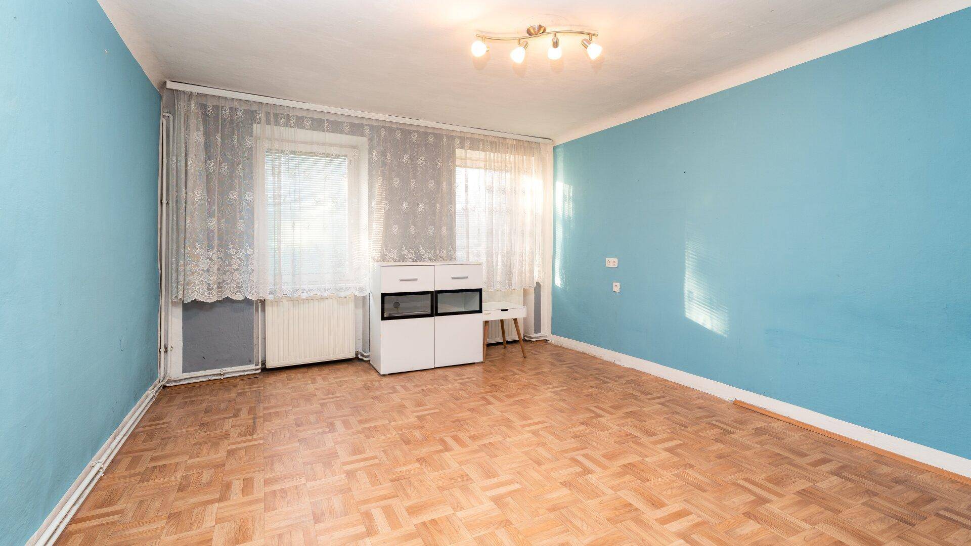 Heller Raum mit blauen Wänden, Parkettboden und großen Fenstern mit Vorhängen, ideal als Wohnzimmer.
