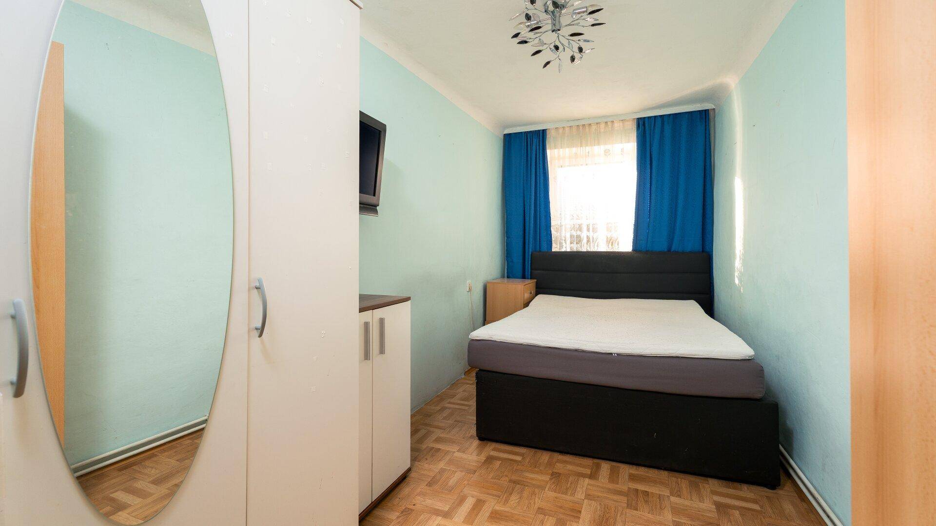 Schlafzimmer mit hellblauen Wänden, Parkettboden und einem Doppelbett, mit natürlichem Lichteinfall.