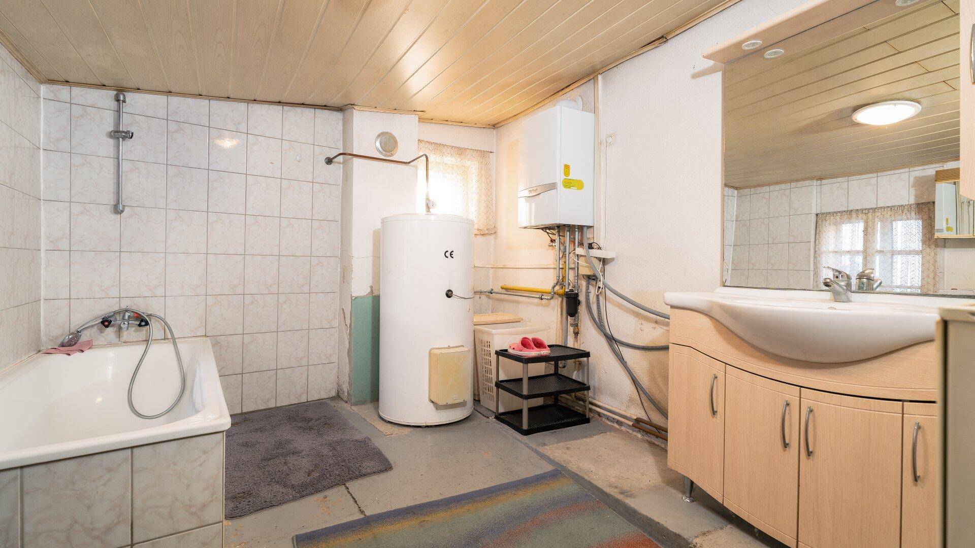 Funktionales Badezimmer mit Badewanne, Waschbecken und Warmwasserboiler in einfacher, aber sauberer Ausstattung.