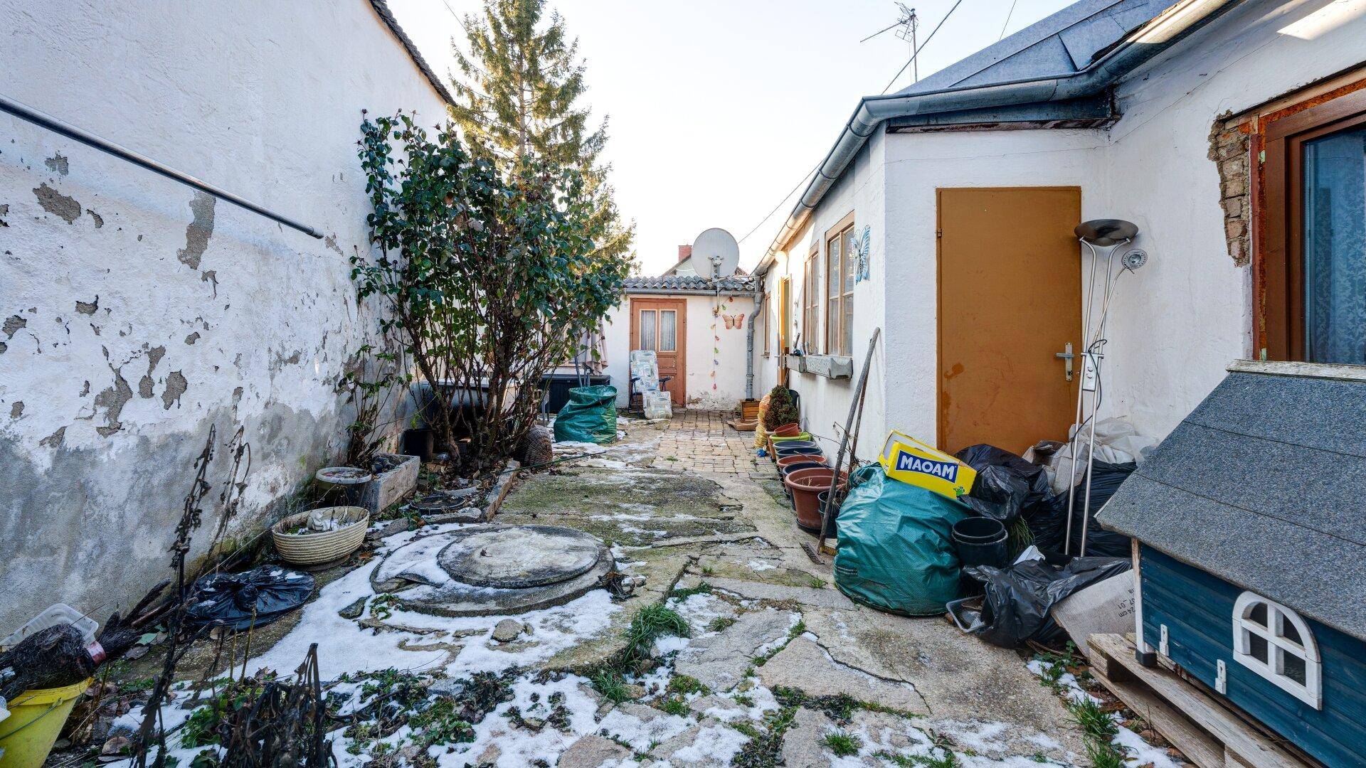 Innenhof mit Schnee, einem Baum und verschiedenen Gegenständen, umgeben von alten Mauern, mit viel Potenzial.