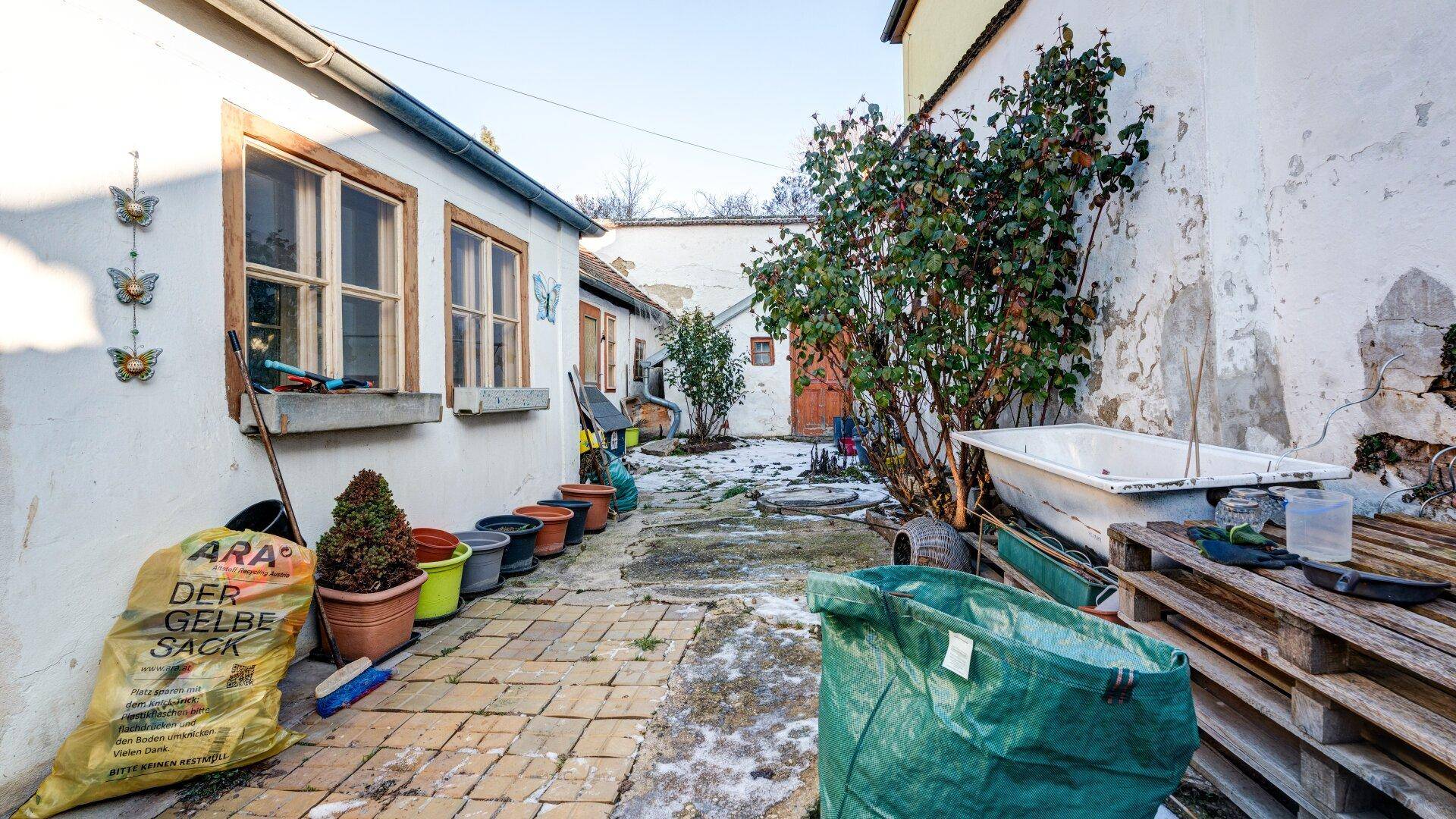 Innenhof mit alten Pflastersteinen, Schnee und einer Badewanne als Pflanzgefäß, rustikal und charmant.