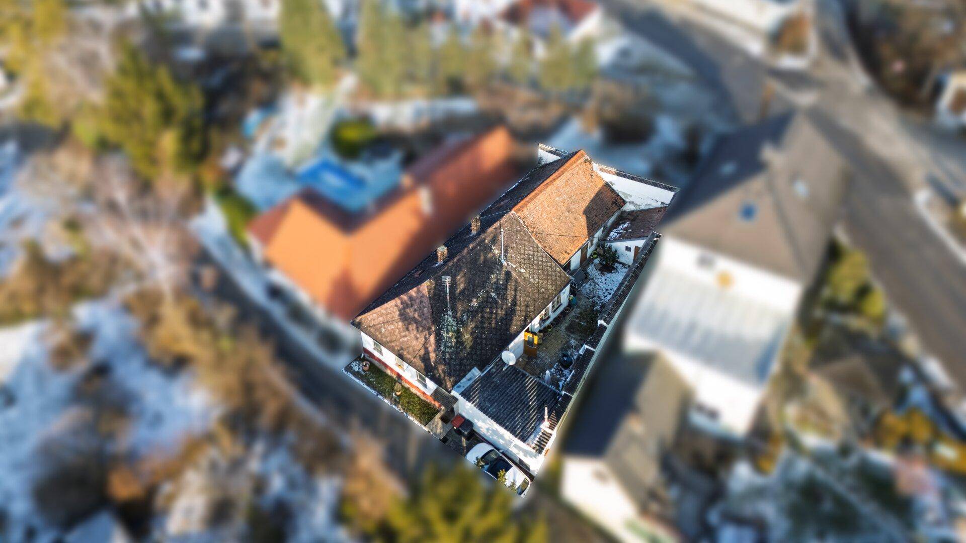 Schräge Luftaufnahme eines Wohnhauses mit Satteldach und verschneiter Umgebung, umgeben von Bäumen.