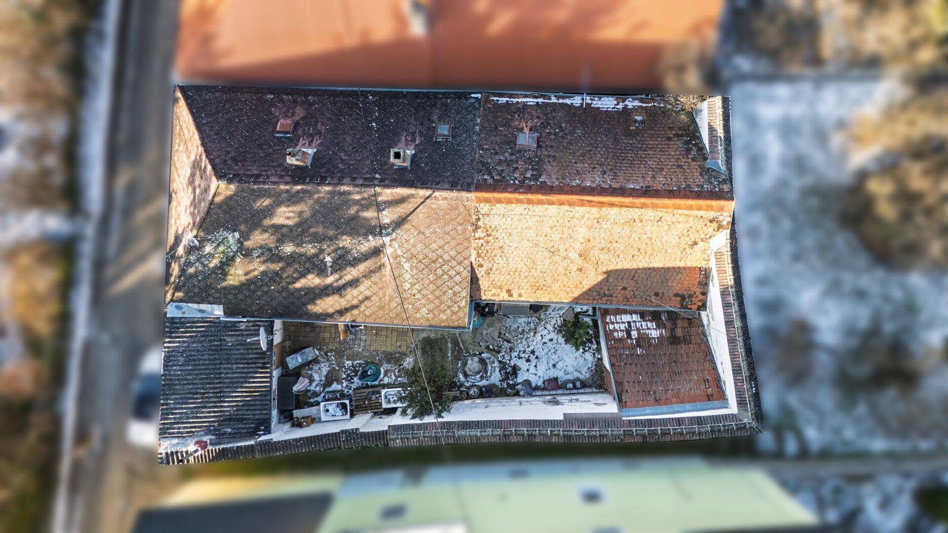 Luftaufnahme eines Gebäudes mit Satteldach und einem kleinen Innenhof, teilweise mit Schnee bedeckt.