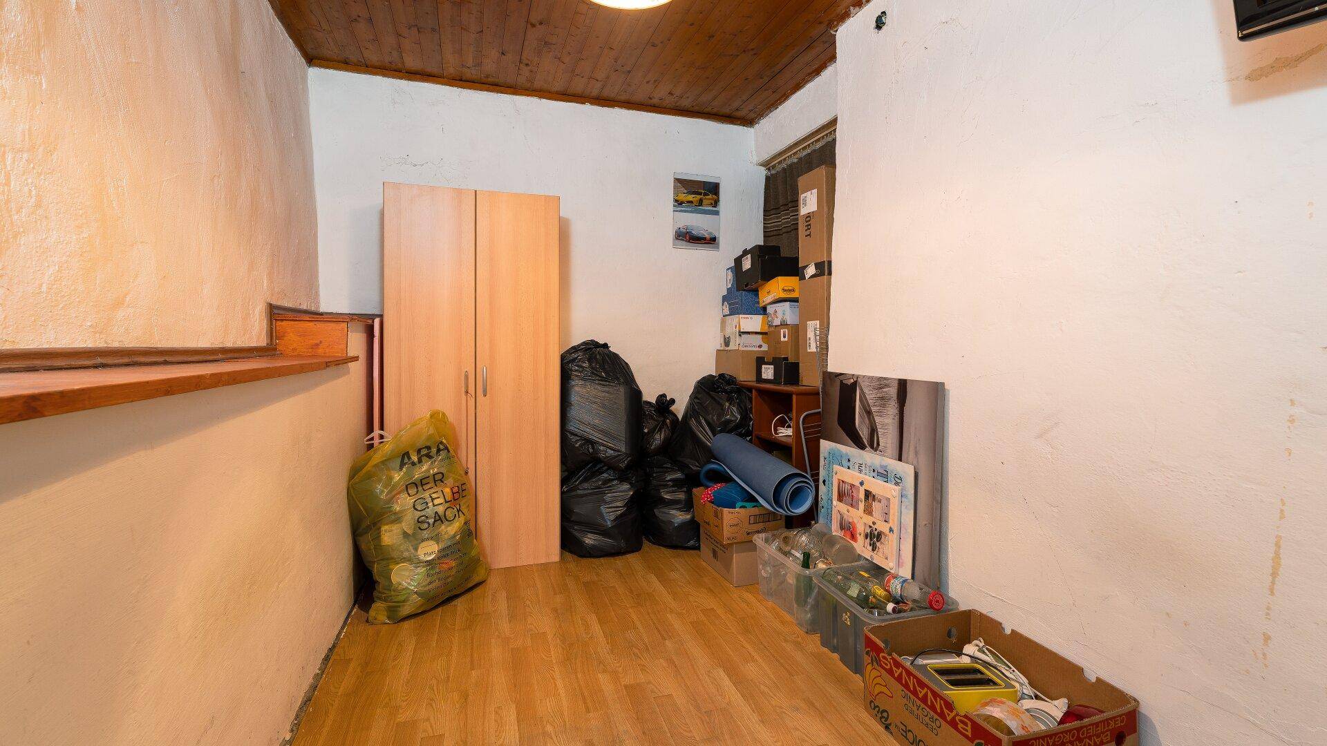 Abstellraum mit Holzdecke und verschiedenen Lagergegenständen, unter der Treppe gelegen, praktisch und geräumig.