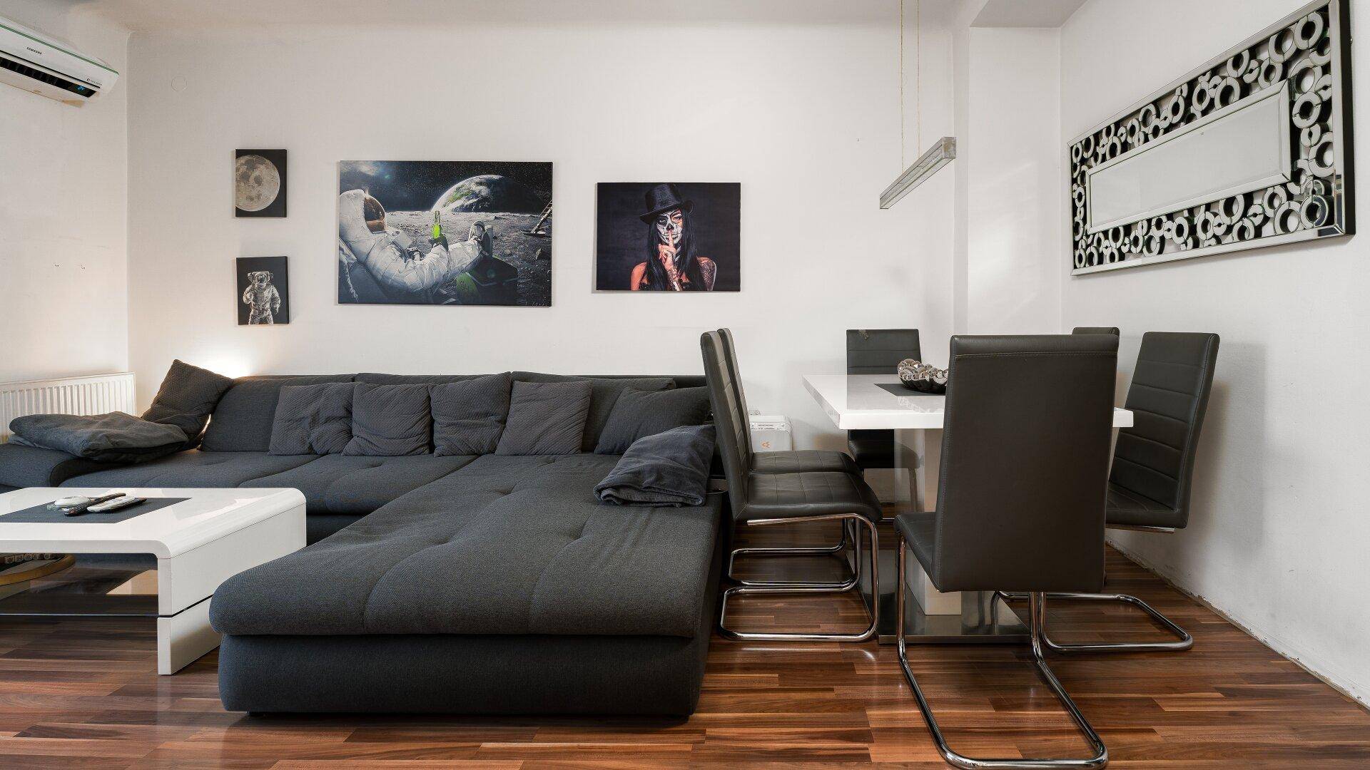 Gemütlicher Wohn- und Essbereich mit dunklem Ecksofa, Esstisch und Holzboden.