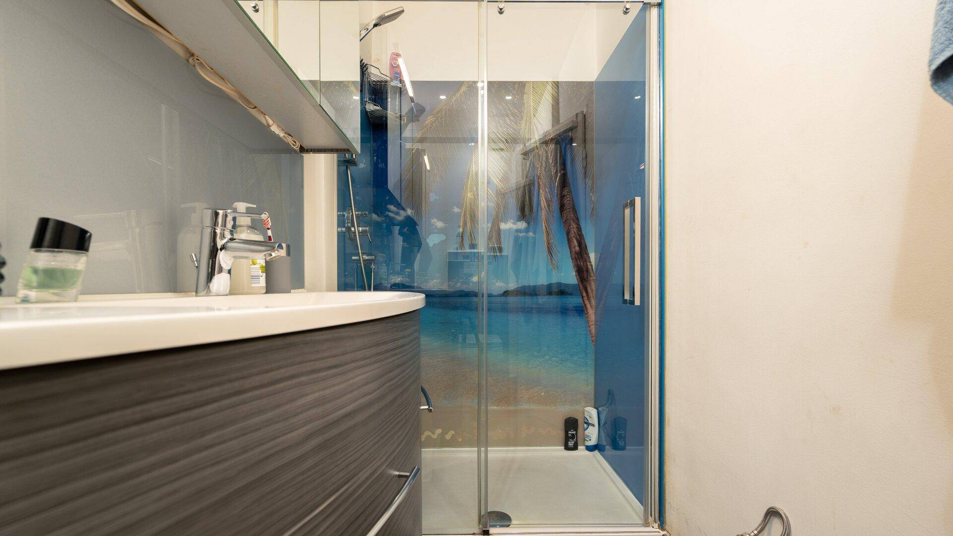 Modernes Badezimmer mit Waschtisch und einer Duschkabine mit tropischem Motiv an der Rückwand.