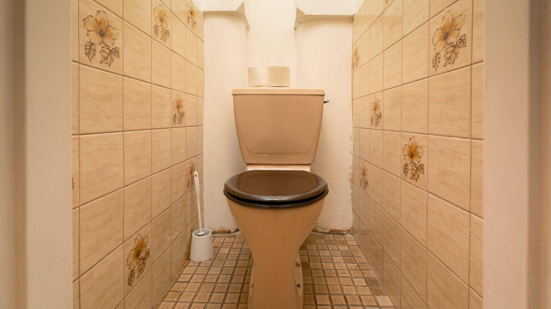 Separate Toilette mit beigefarbenen Fliesen, floralem Muster und einem einfachen WC.