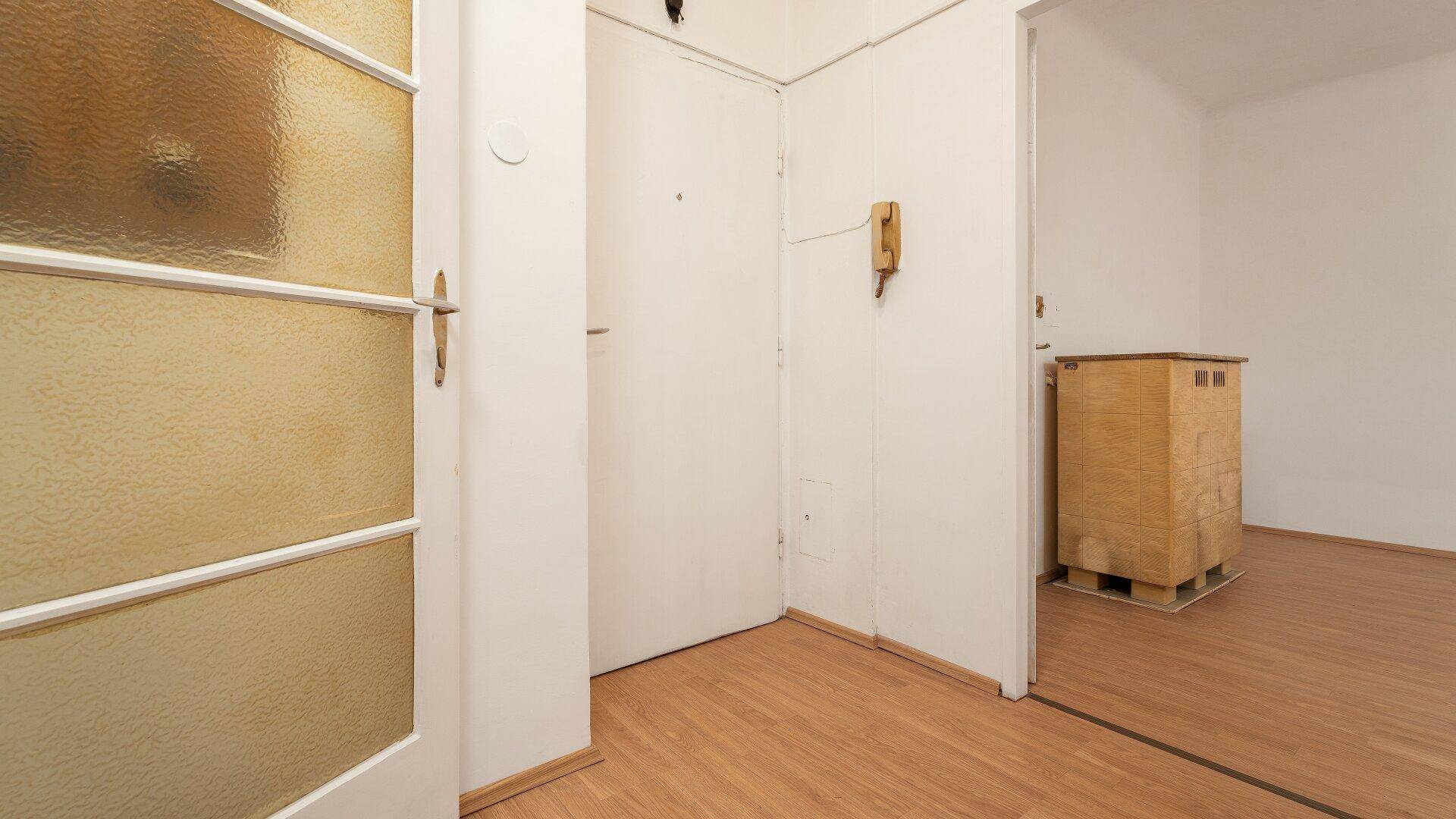Eingangsbereich mit einer Tür mit Milchglas, einem alten Telefon und Blick in einen weiteren Raum.