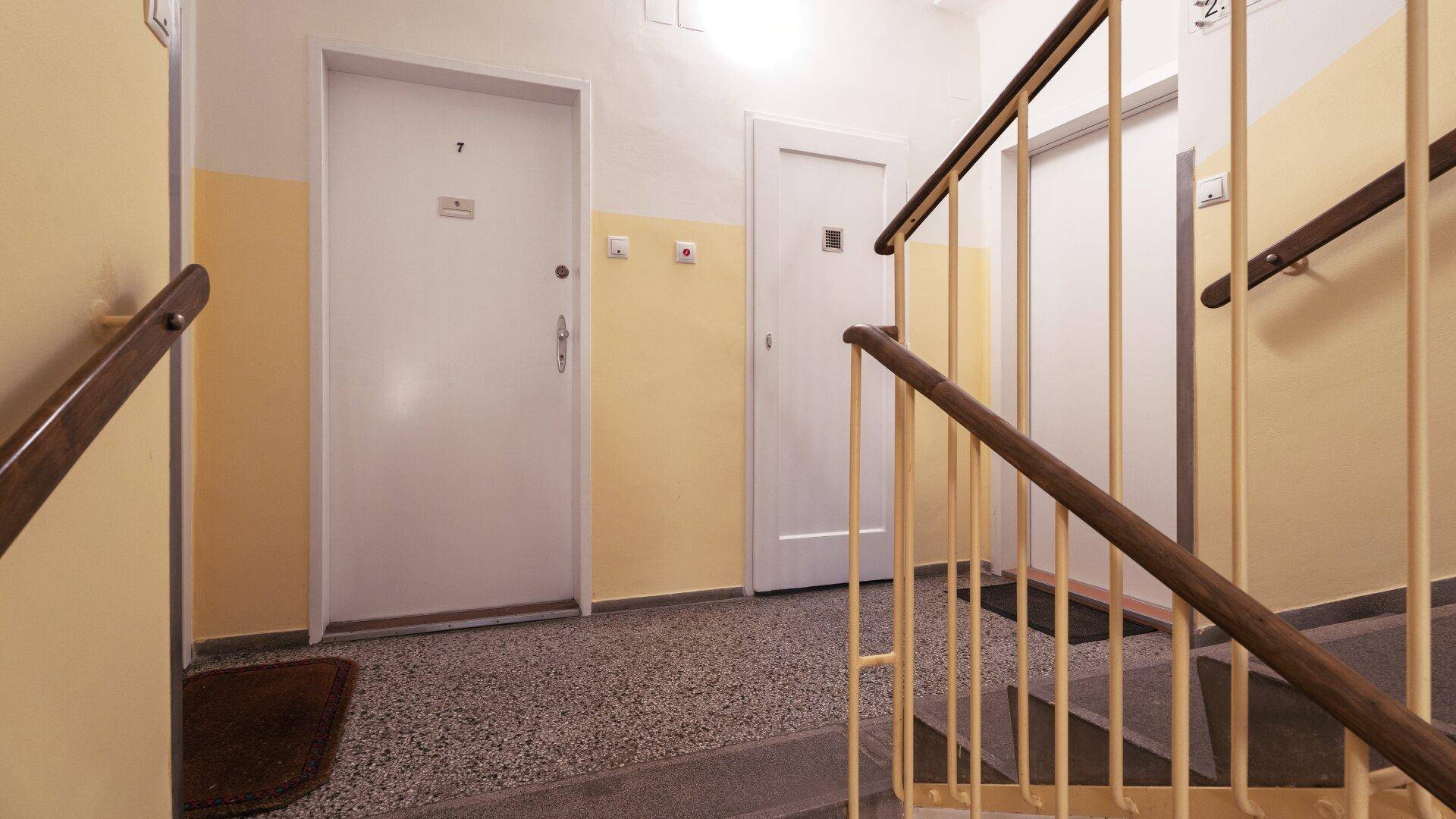 Treppenabsatz mit zwei Wohnungstüren, gelben Wänden und einem Terrazzoboden im Mehrfamilienhaus.