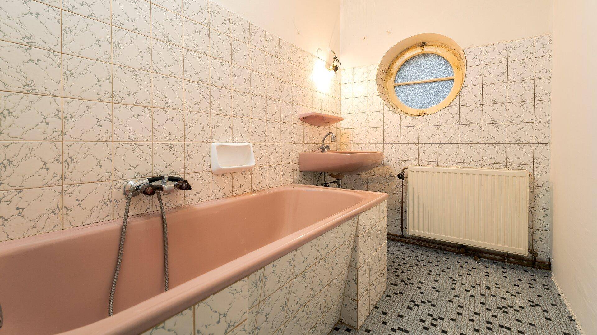 Badezimmer mit rosa Badewanne, passendem Waschbecken und gemusterten Fliesen an Wänden und Boden.