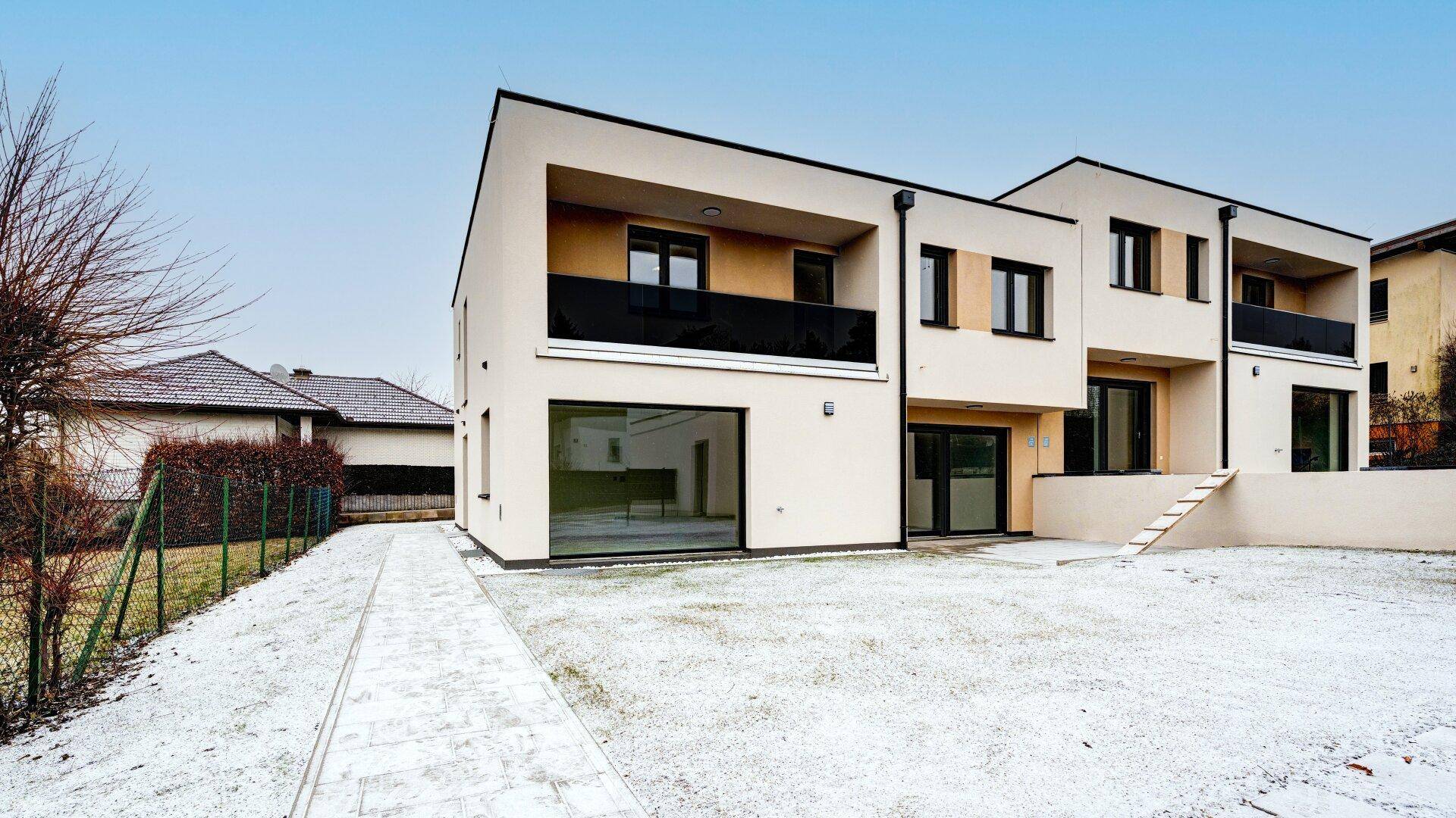 Moderne Reihenhäuser mit großen Fenstern und Balkonen, umgeben von einer verschneiten Rasenfläche.