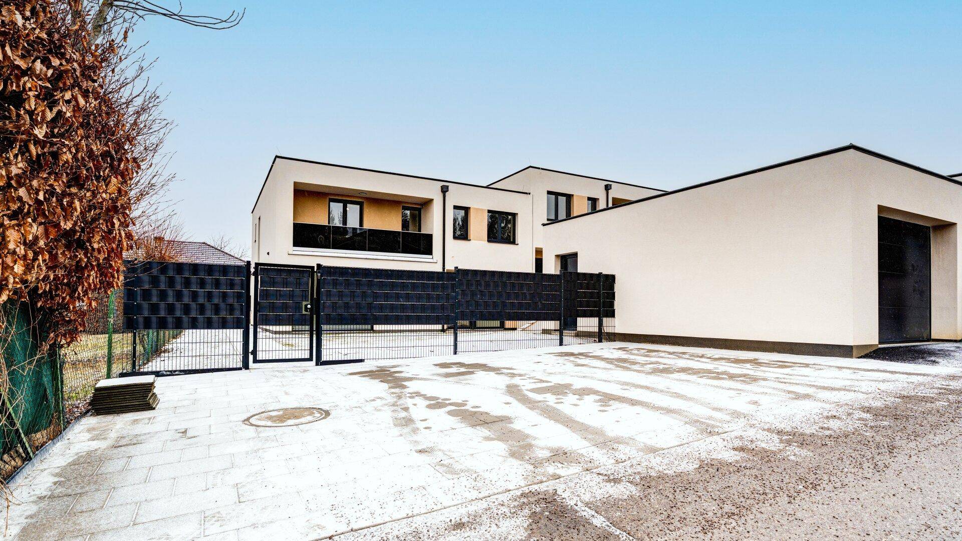 Neubau-Reihenhäuser mit moderner Architektur, Garage und Zufahrt, umgeben von einem Zaun.